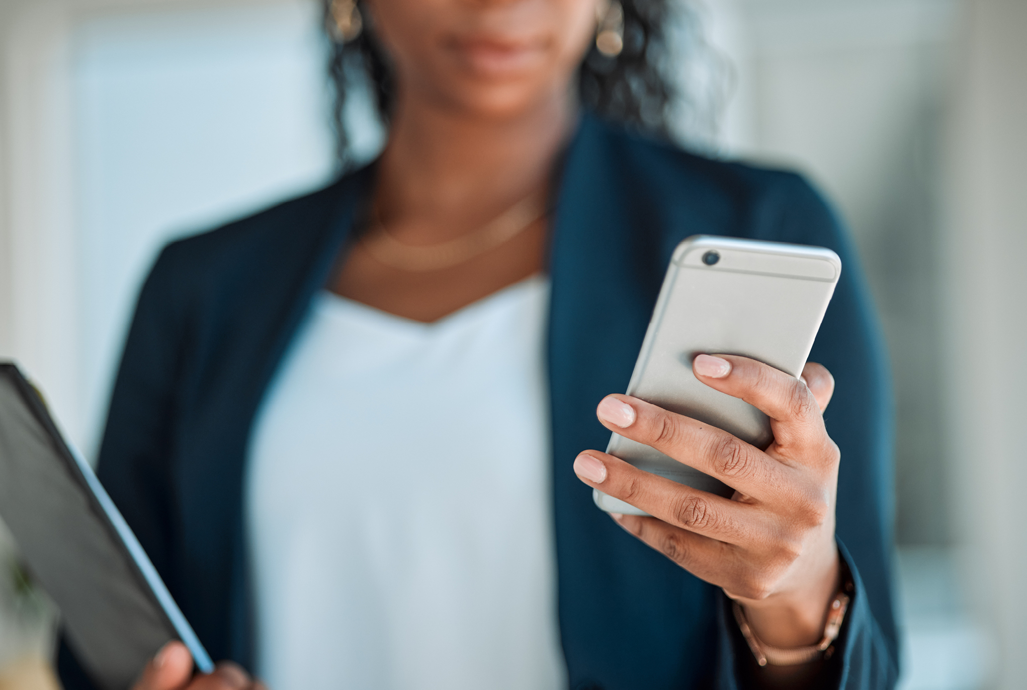A woman in business attire holding a tablet and a phone