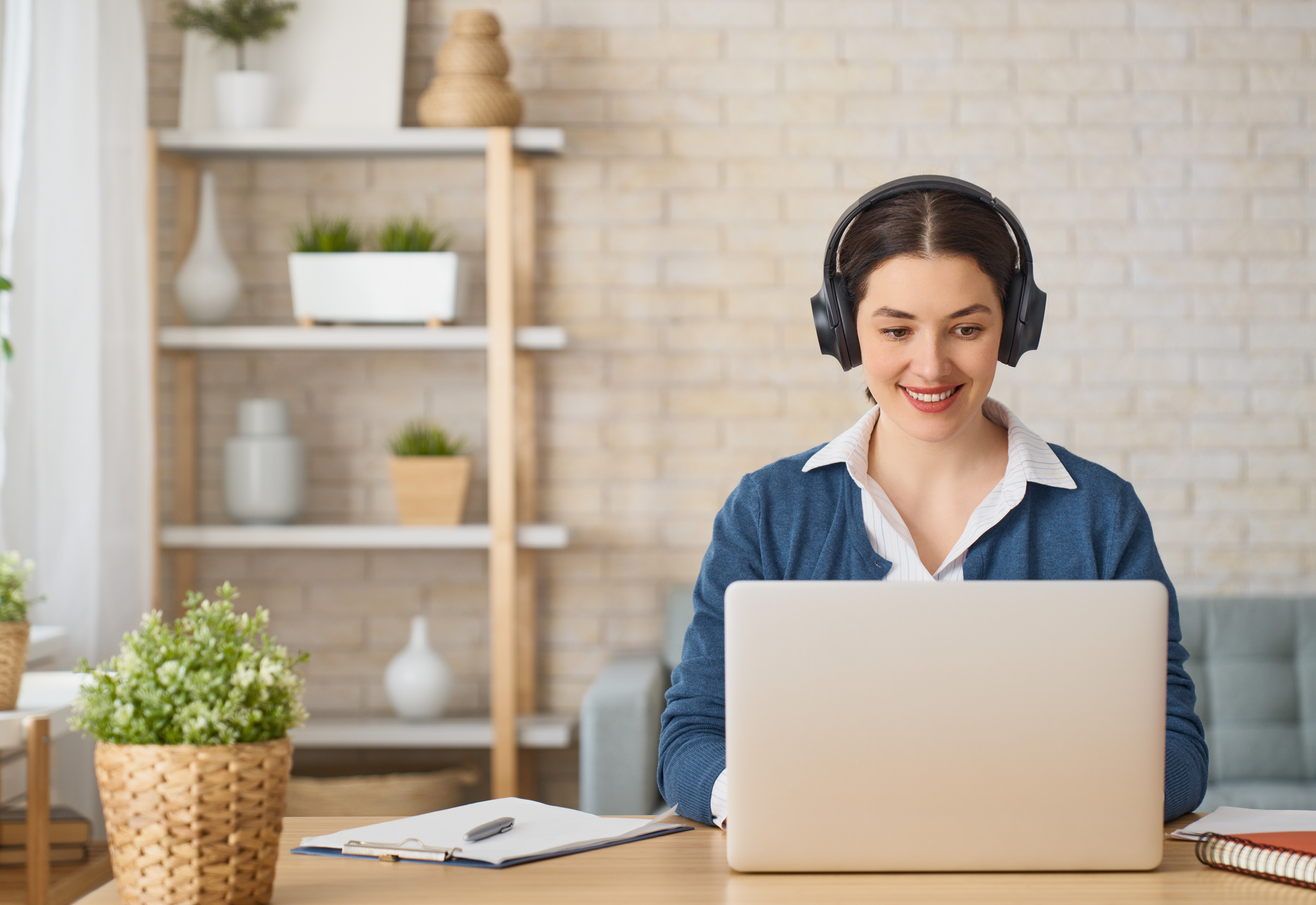 A woman sitting at a desk using a laptop and wearing headphones