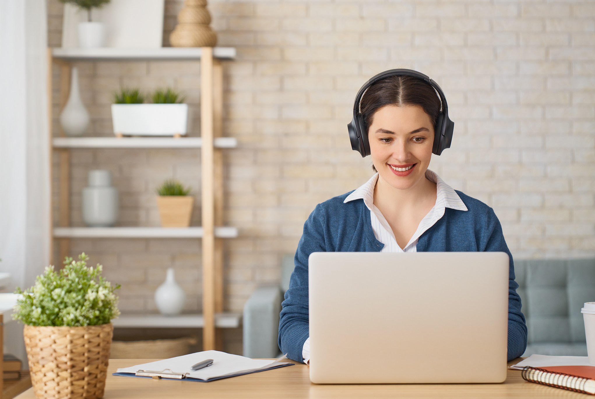 A woman sitting at a desk using a laptop and wearing headphones