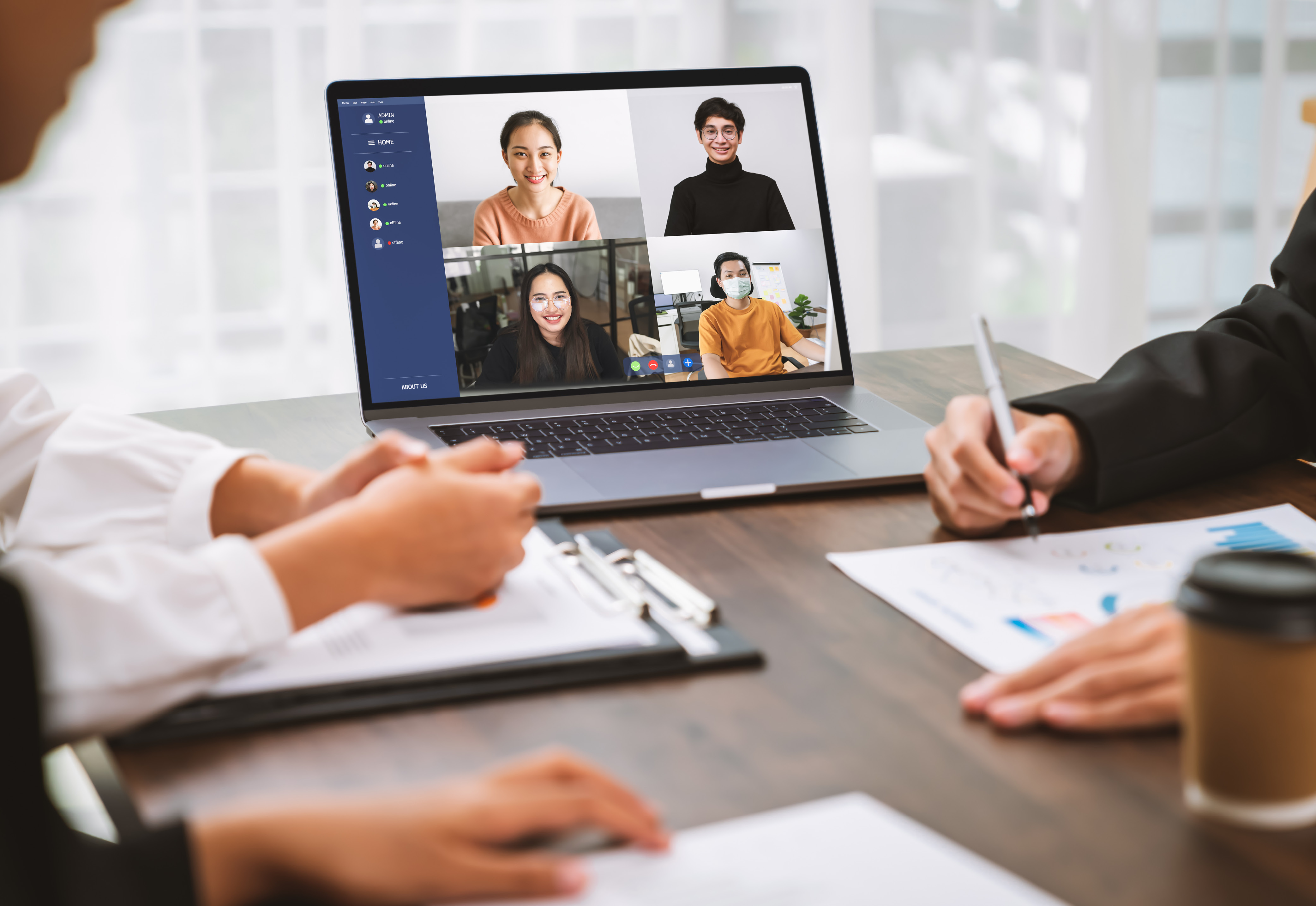 A group of people sitting at a table with a laptop open that has a group of people calling in virtually