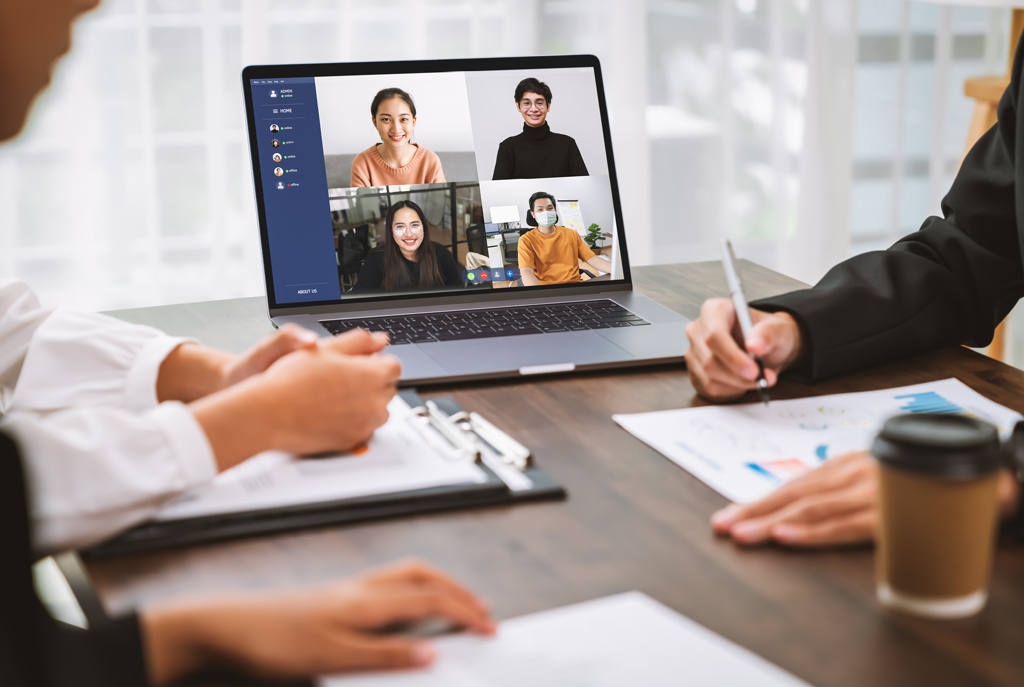 A group of people sitting at a table with a laptop open that has a group of people calling in virtually