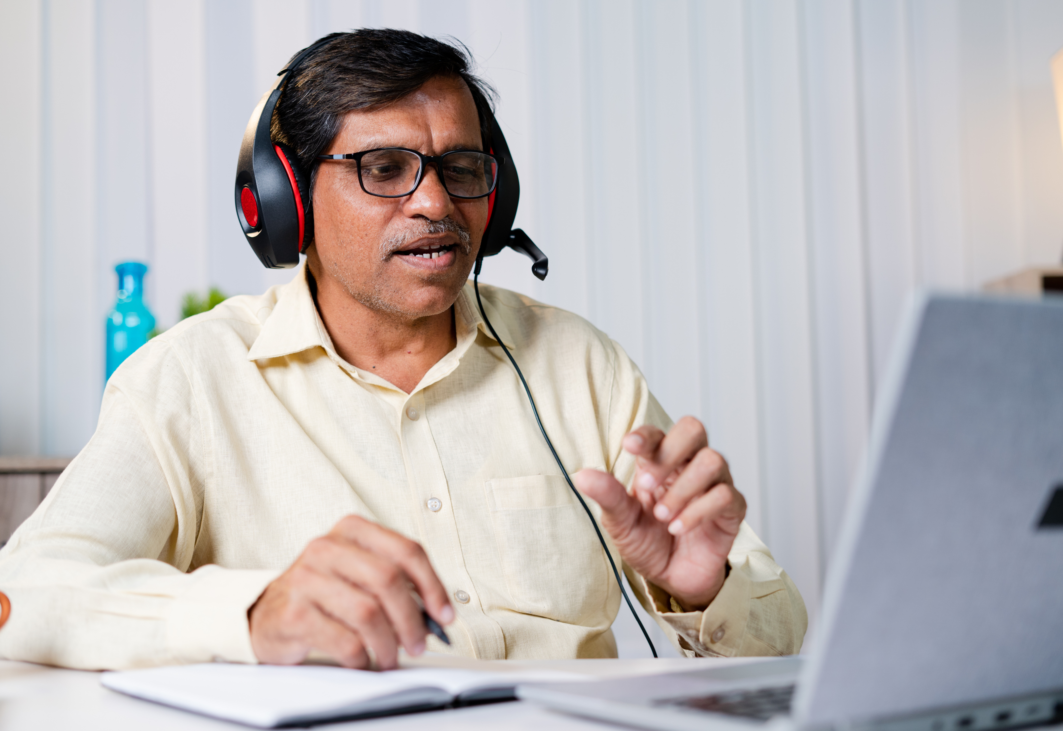 A man wearing headphones sitting with an open notebook and laptop