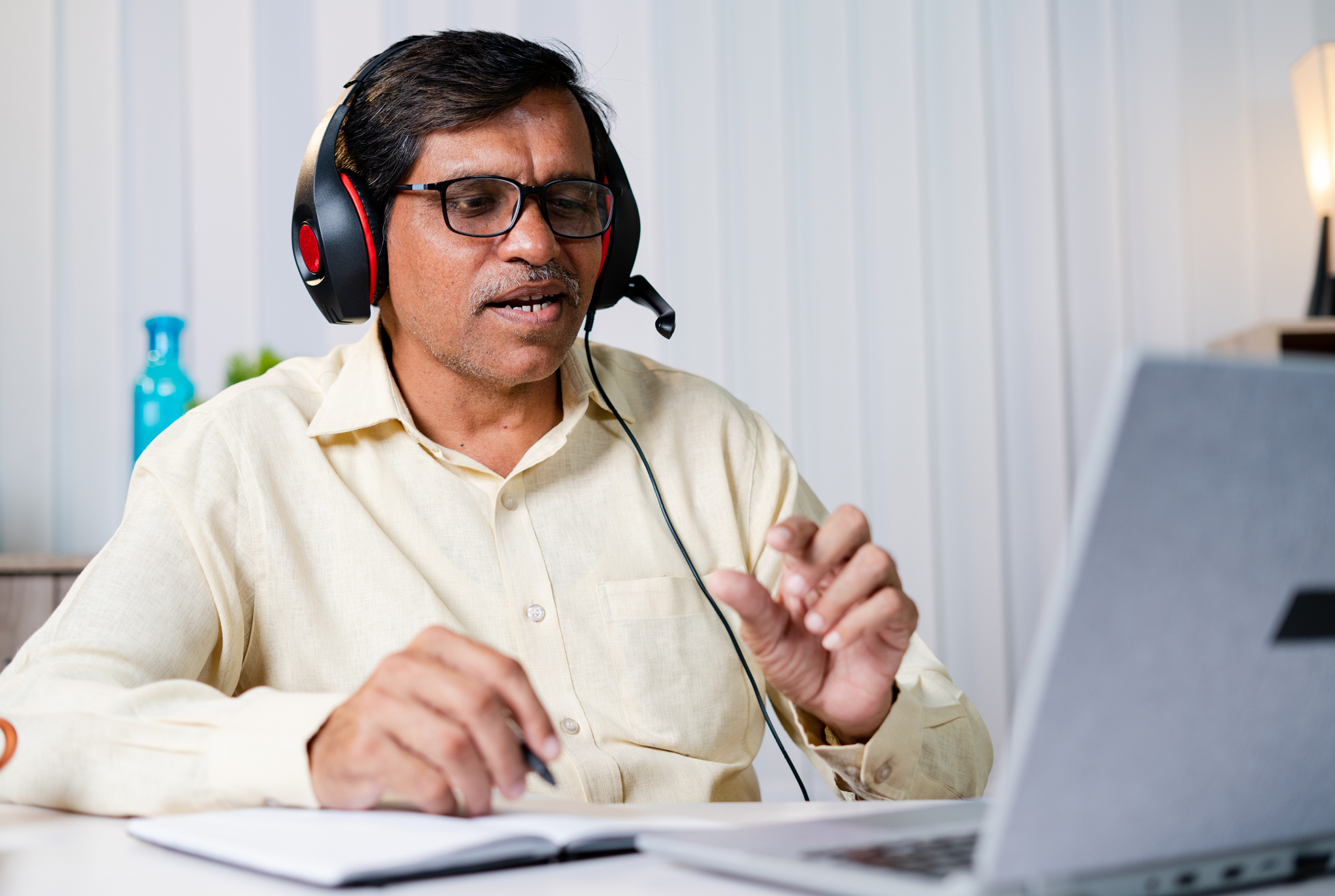 A man wearing headphones sitting with an open notebook and laptop