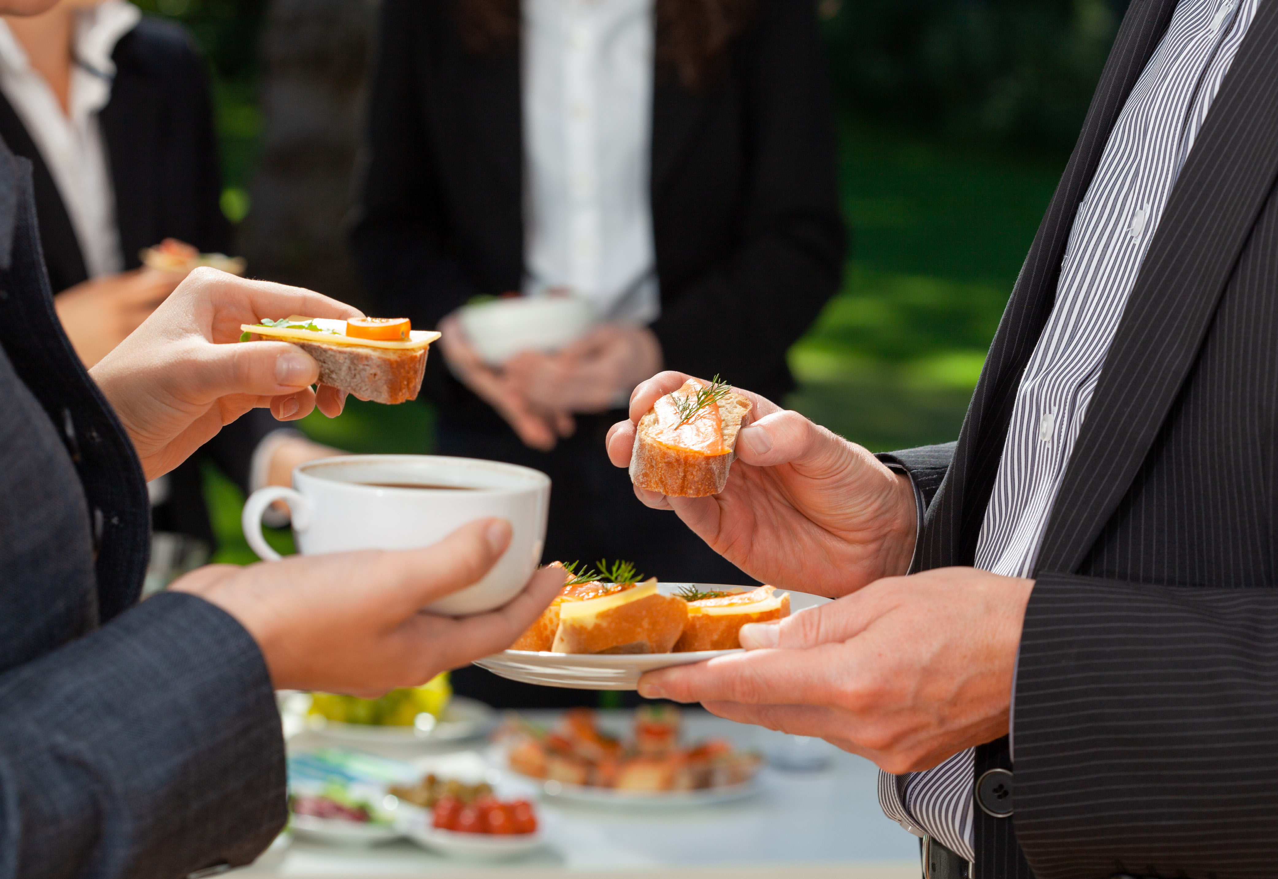 People in business attire holding plates of food and cups of coffee