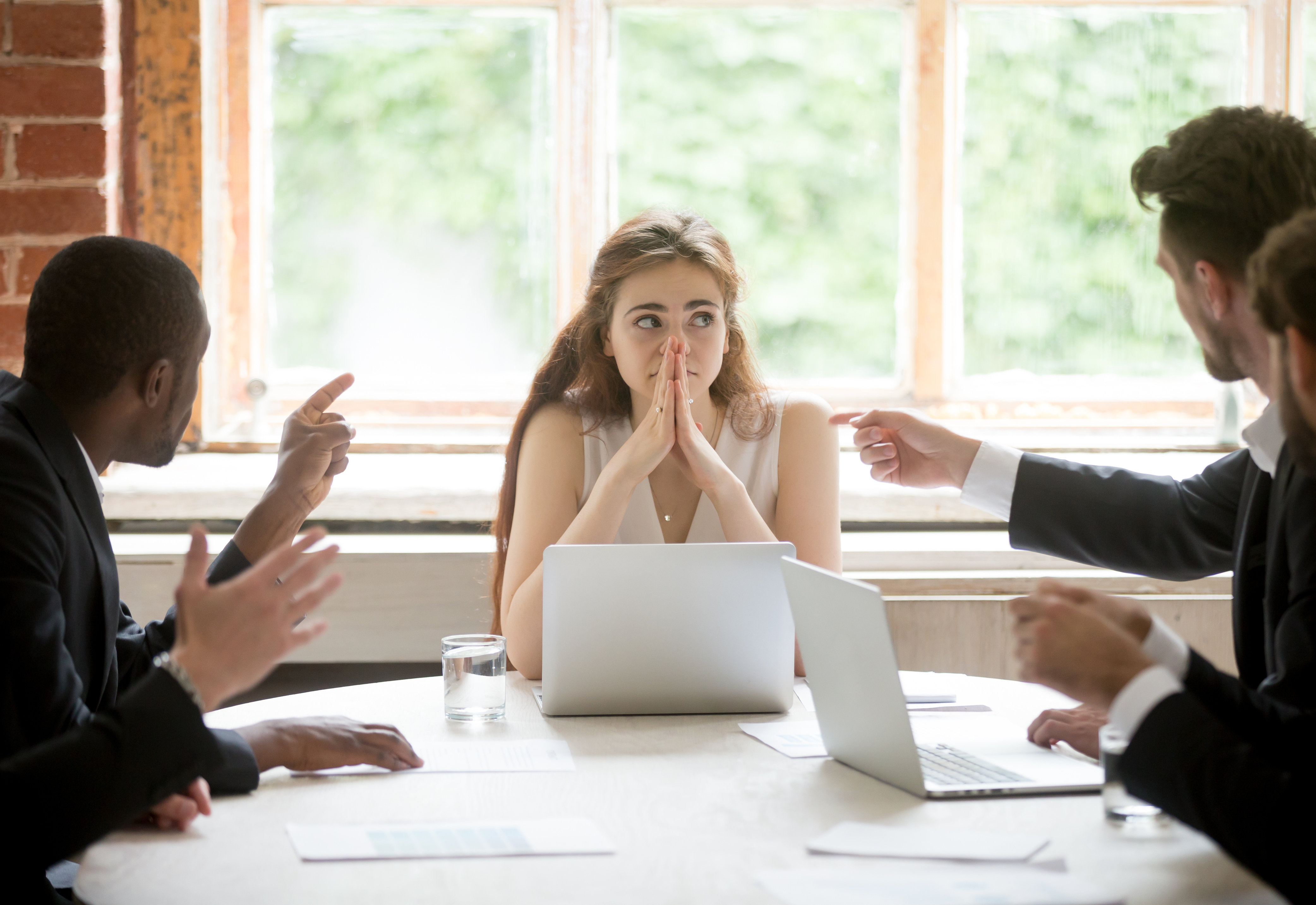 A group of people sitting at a table and pointing fingers at someone