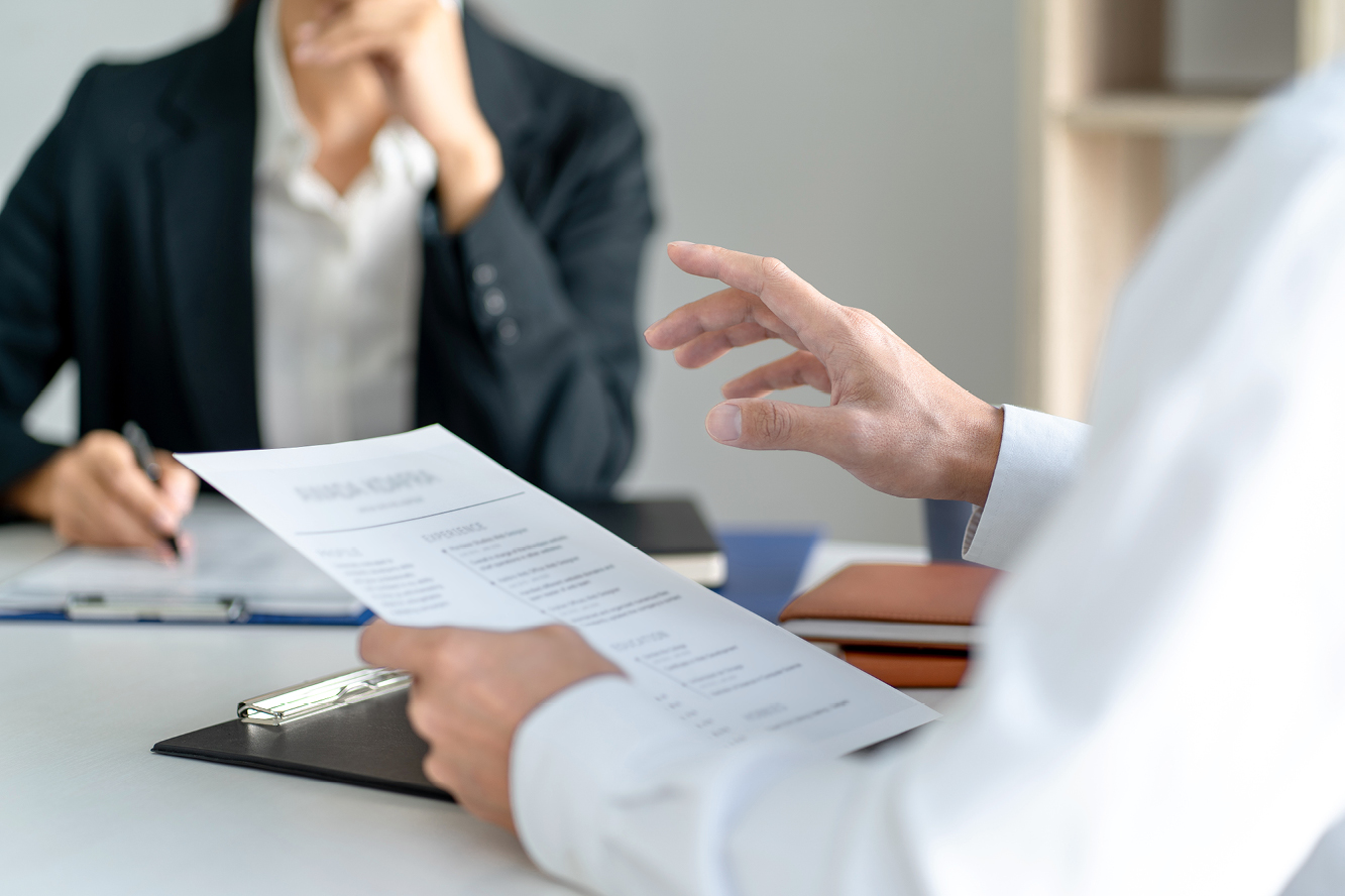 Two people in business attire sitting together, with one person holding a resume 
