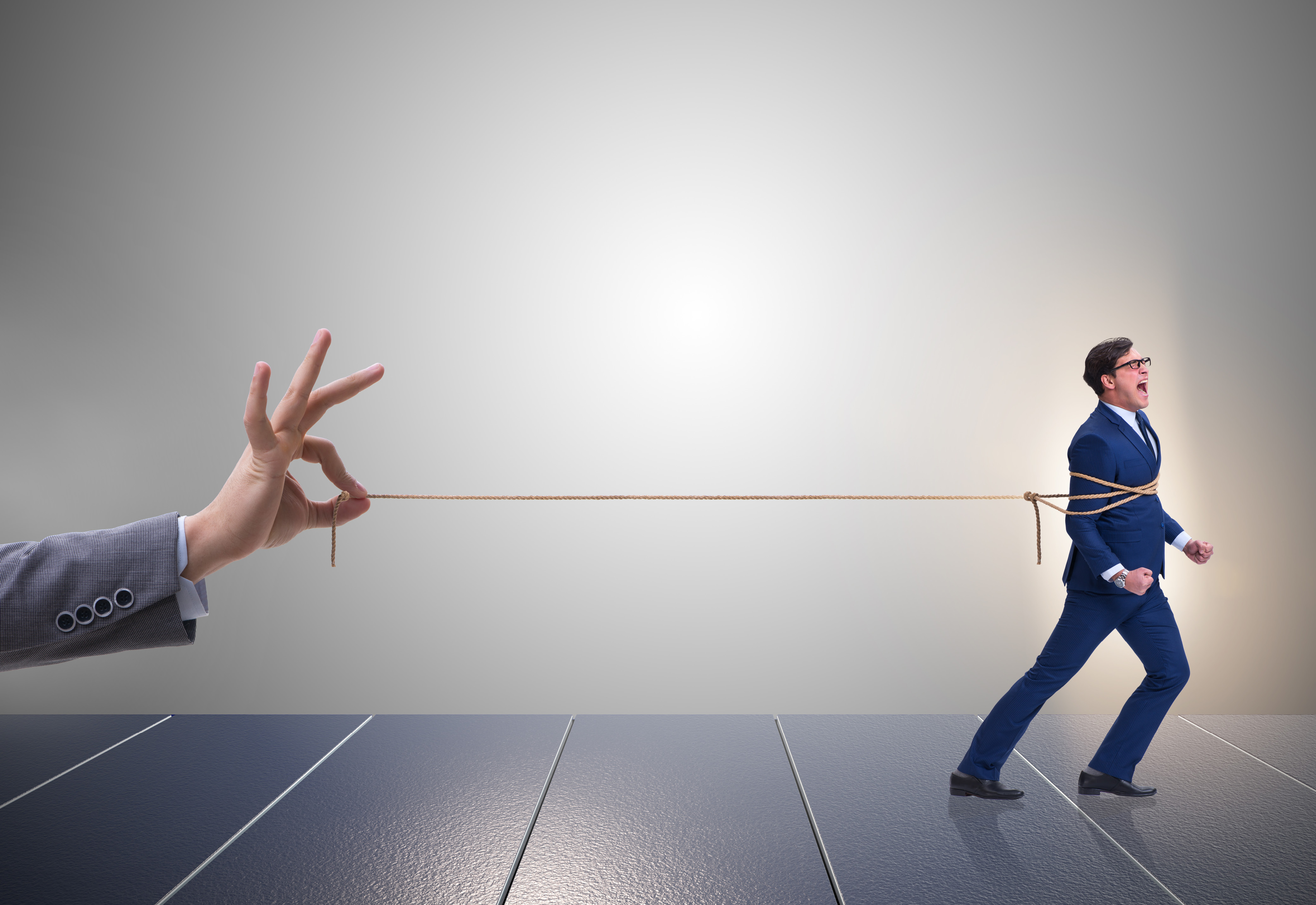A person's hand holding a rope tied around a man in business attire