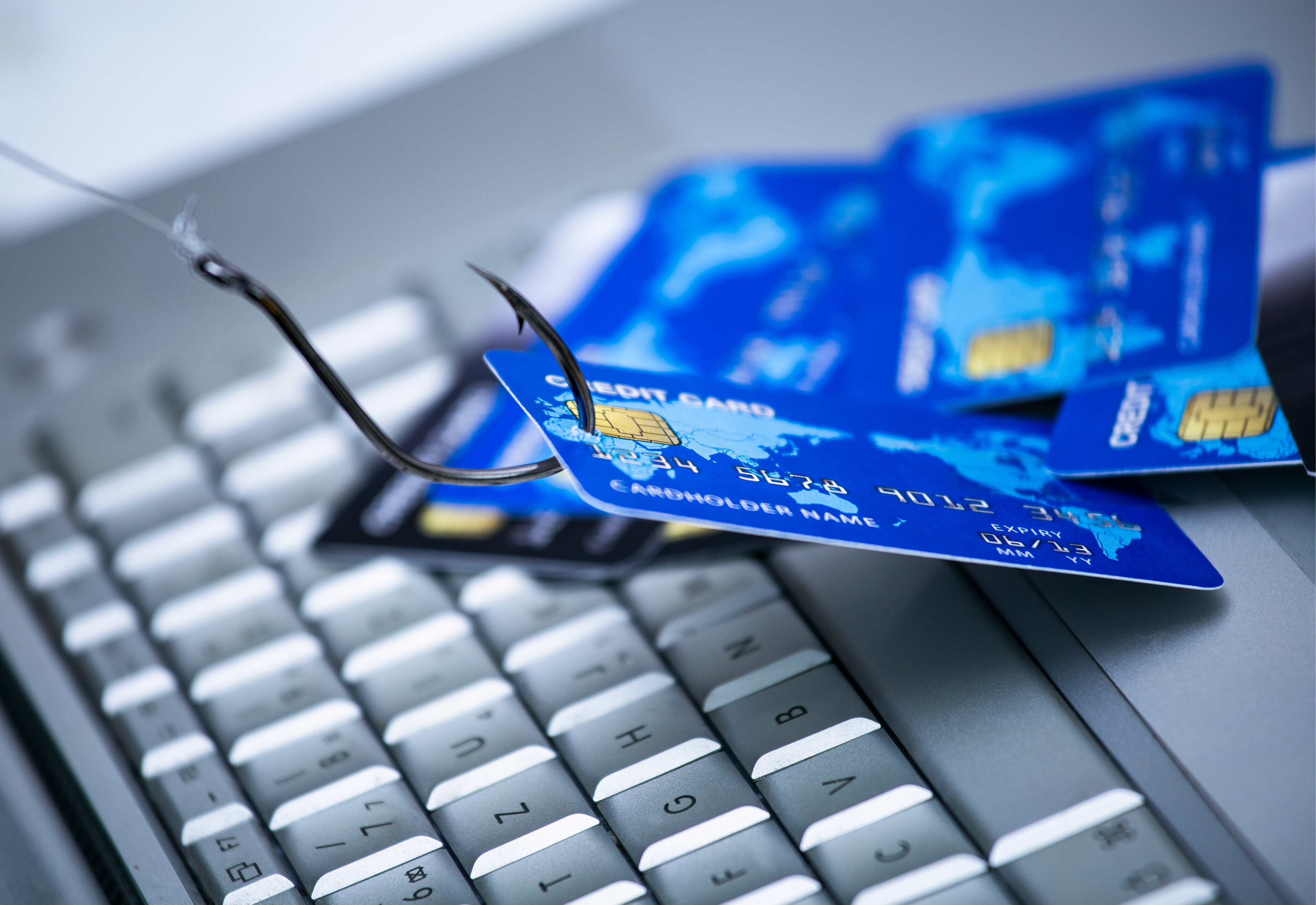 A credit card on top of a laptop keyboard with a fishing hook in it