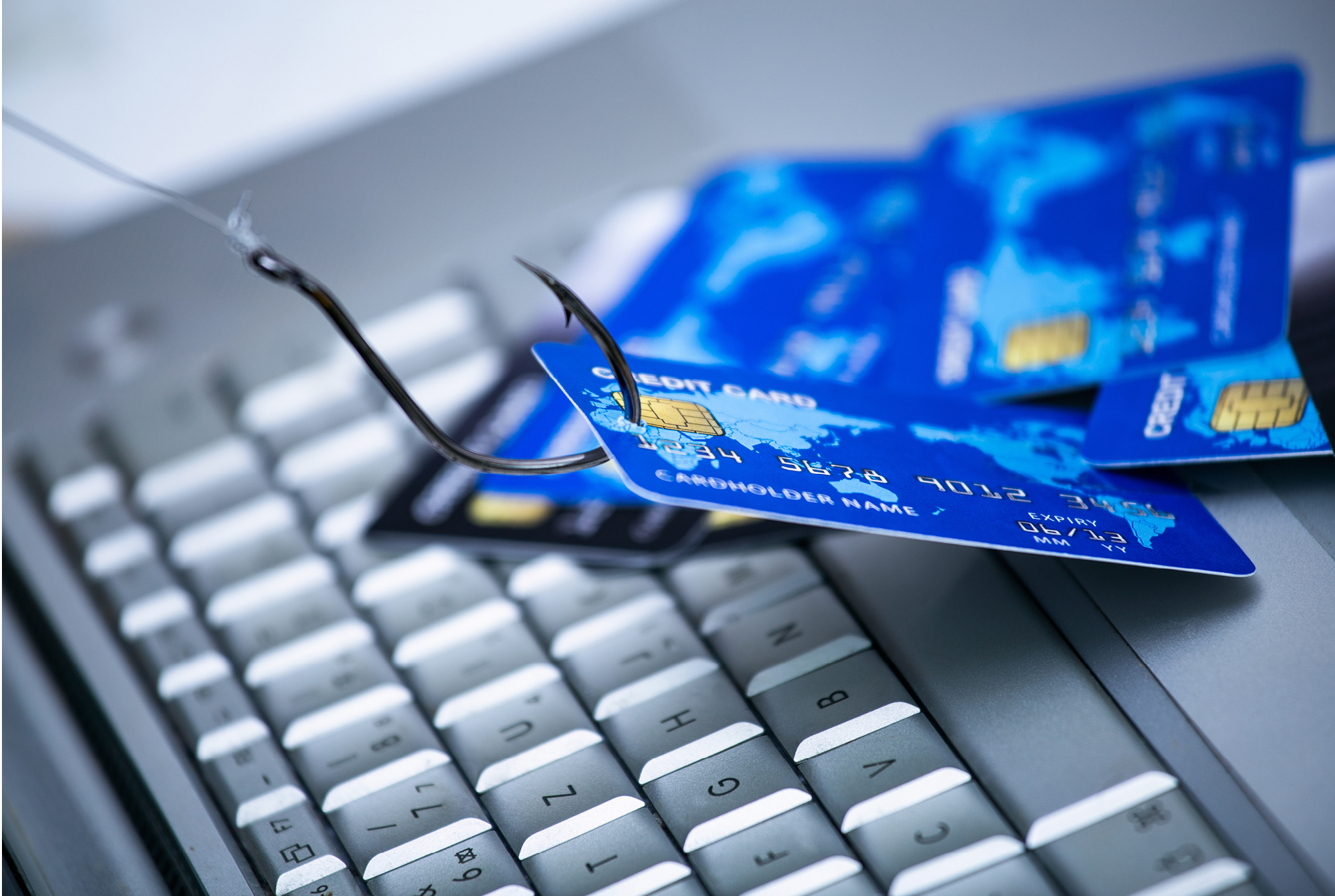 A credit card on top of a laptop keyboard with a fishing hook in it