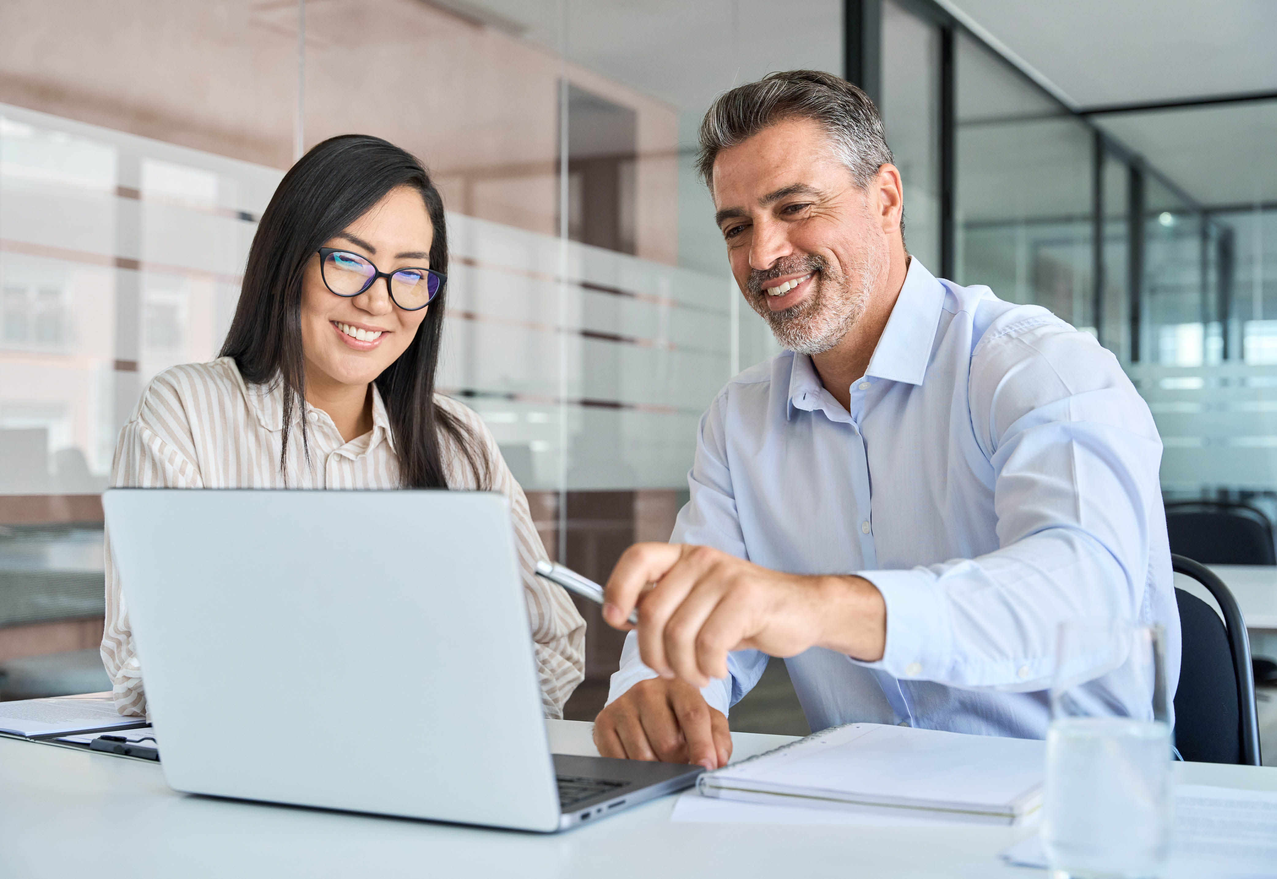 A woman and a man dressed in business attire looking at a laptop together