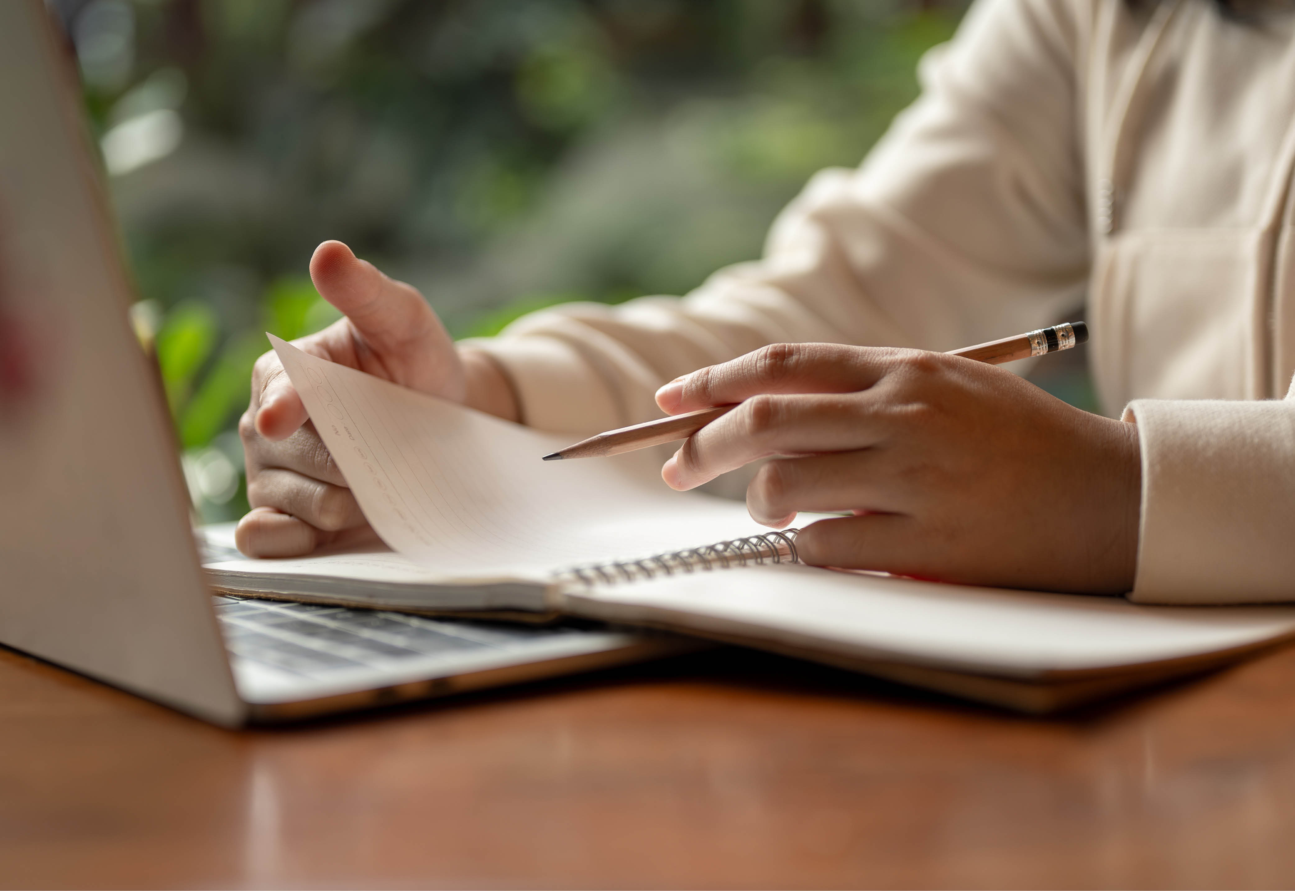 A person sitting behind a laptop taking notes in their notebook. 