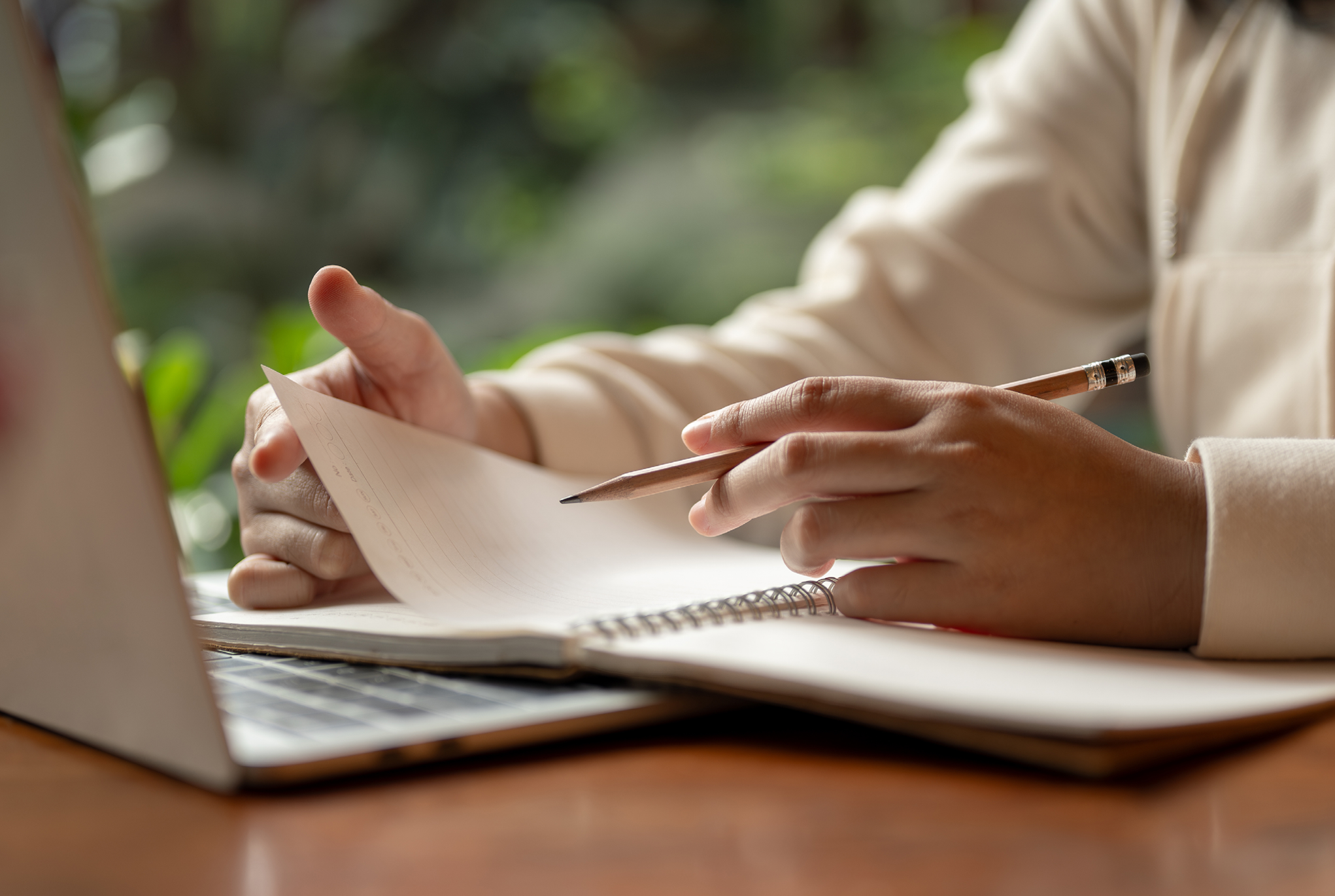 A person sitting behind a laptop taking notes in their notebook. 