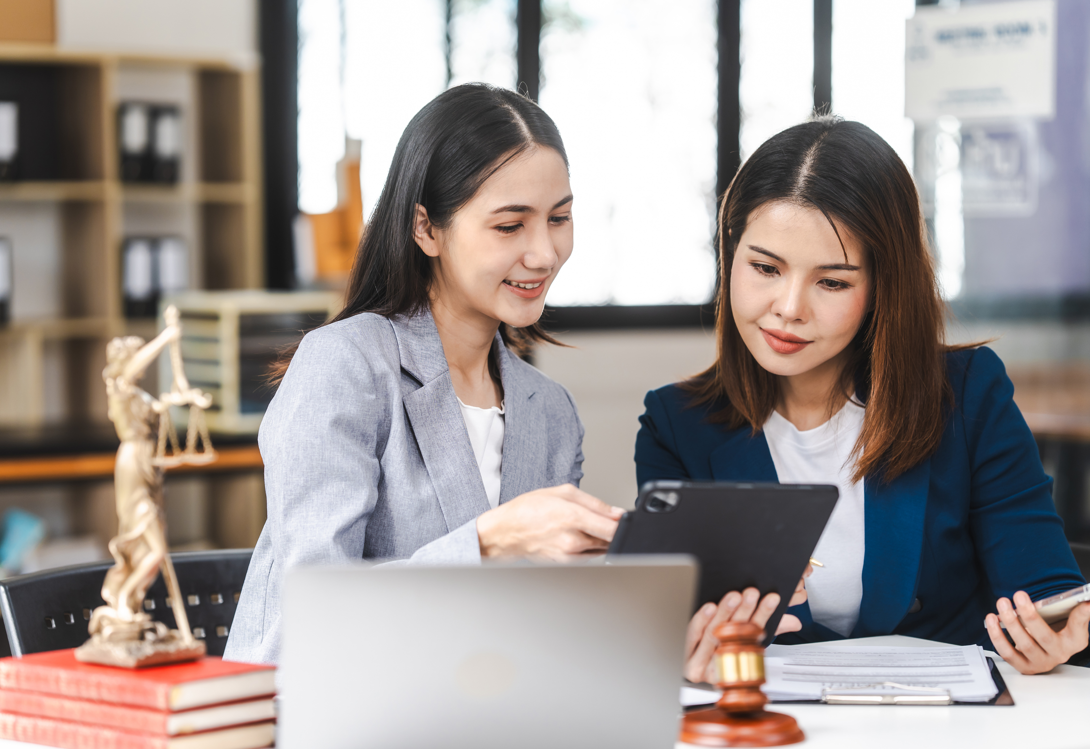 Two women dressed in business attire looking at a tablet together