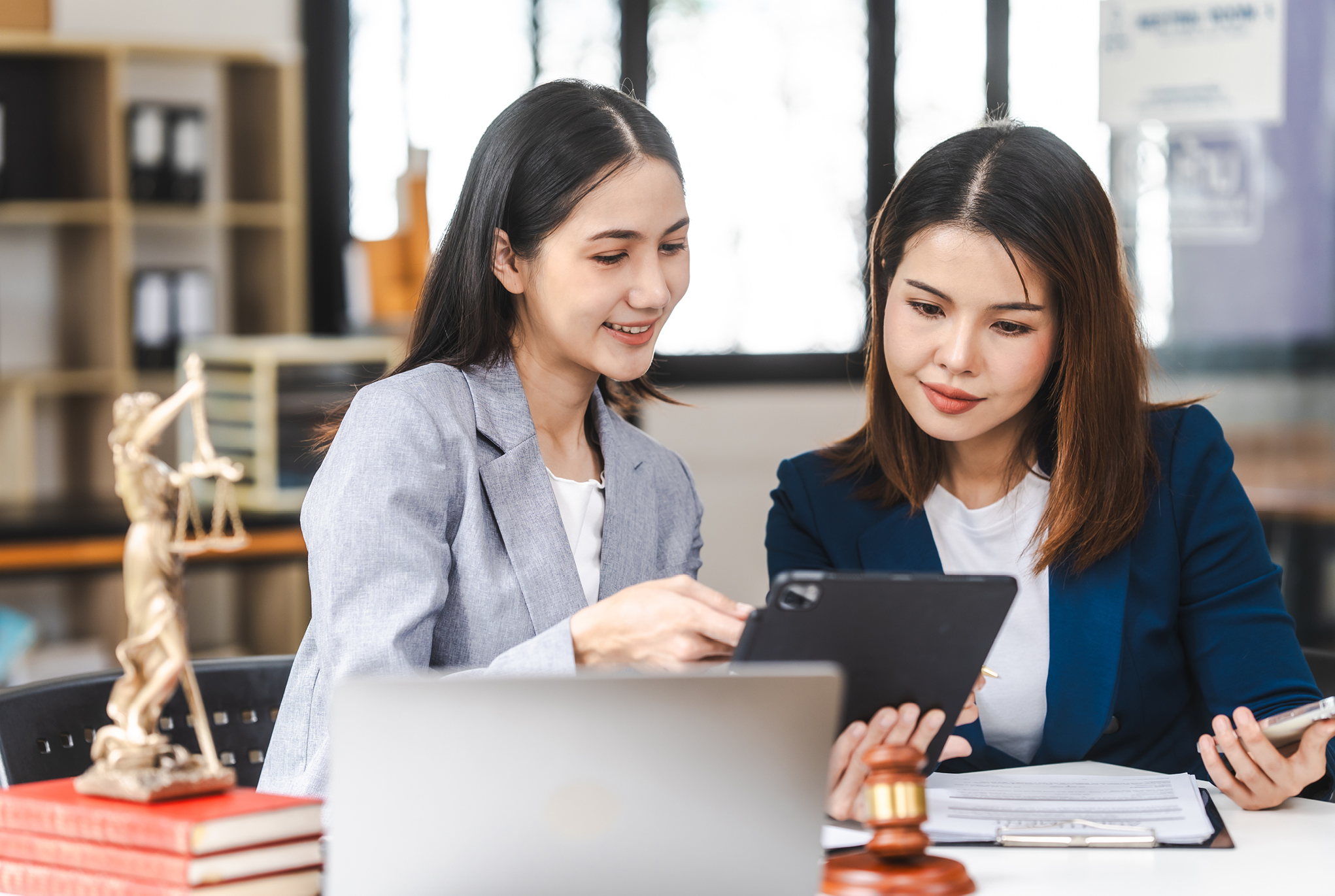 Two women dressed in business attire looking at a tablet together