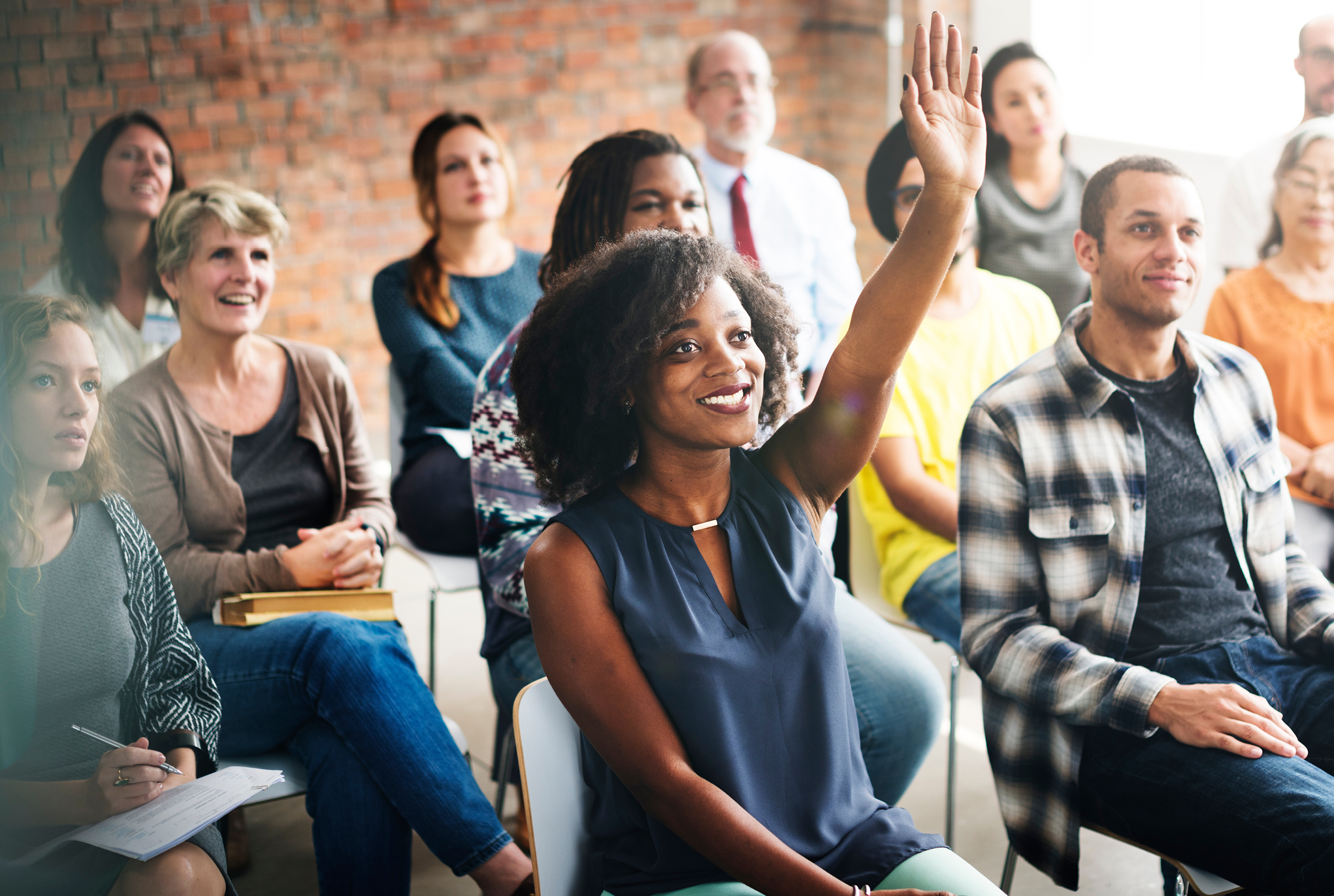 A group of people sitting in chairs with one person raising their hand