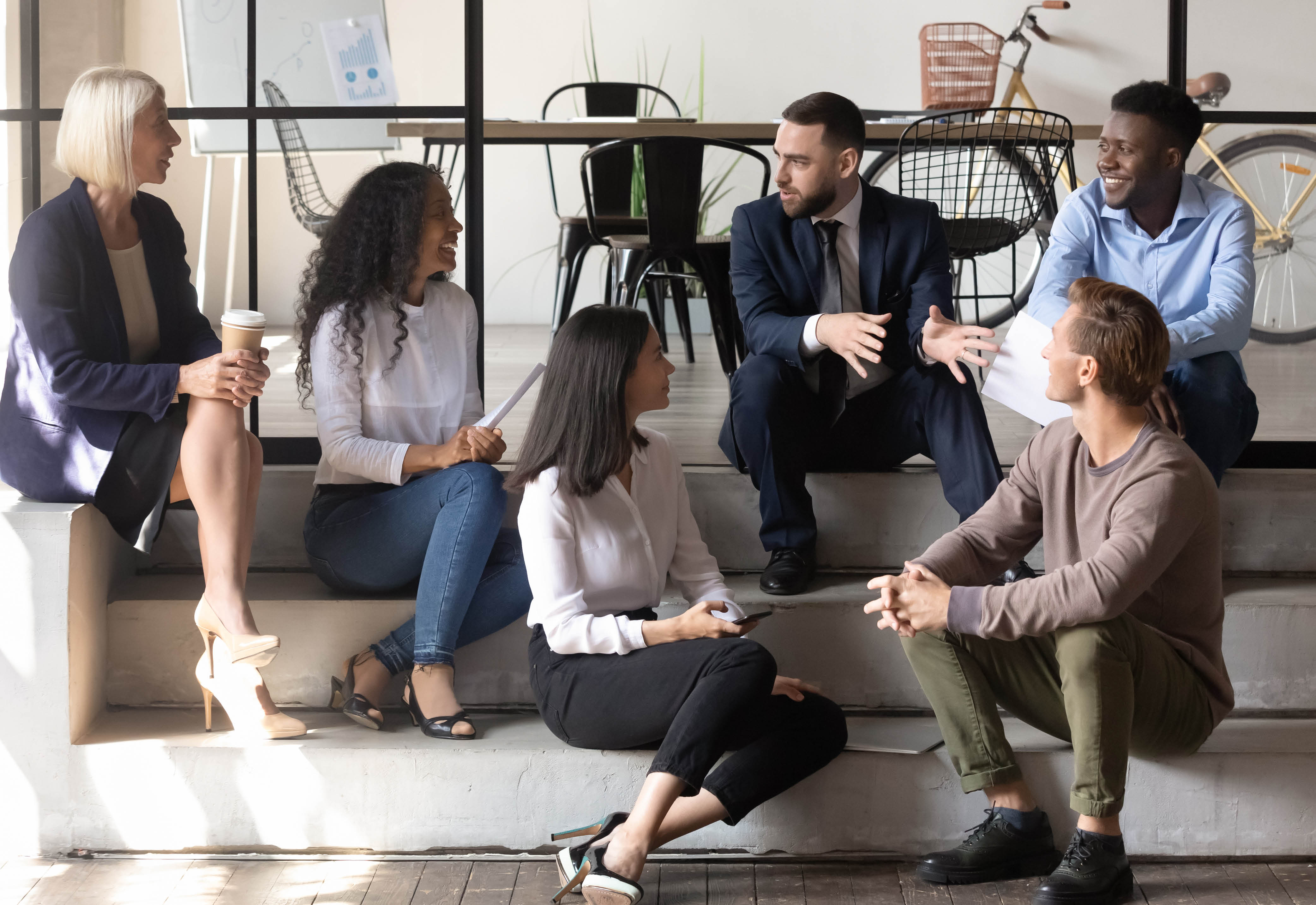 A group of employees sitting on steps talking to each other. 