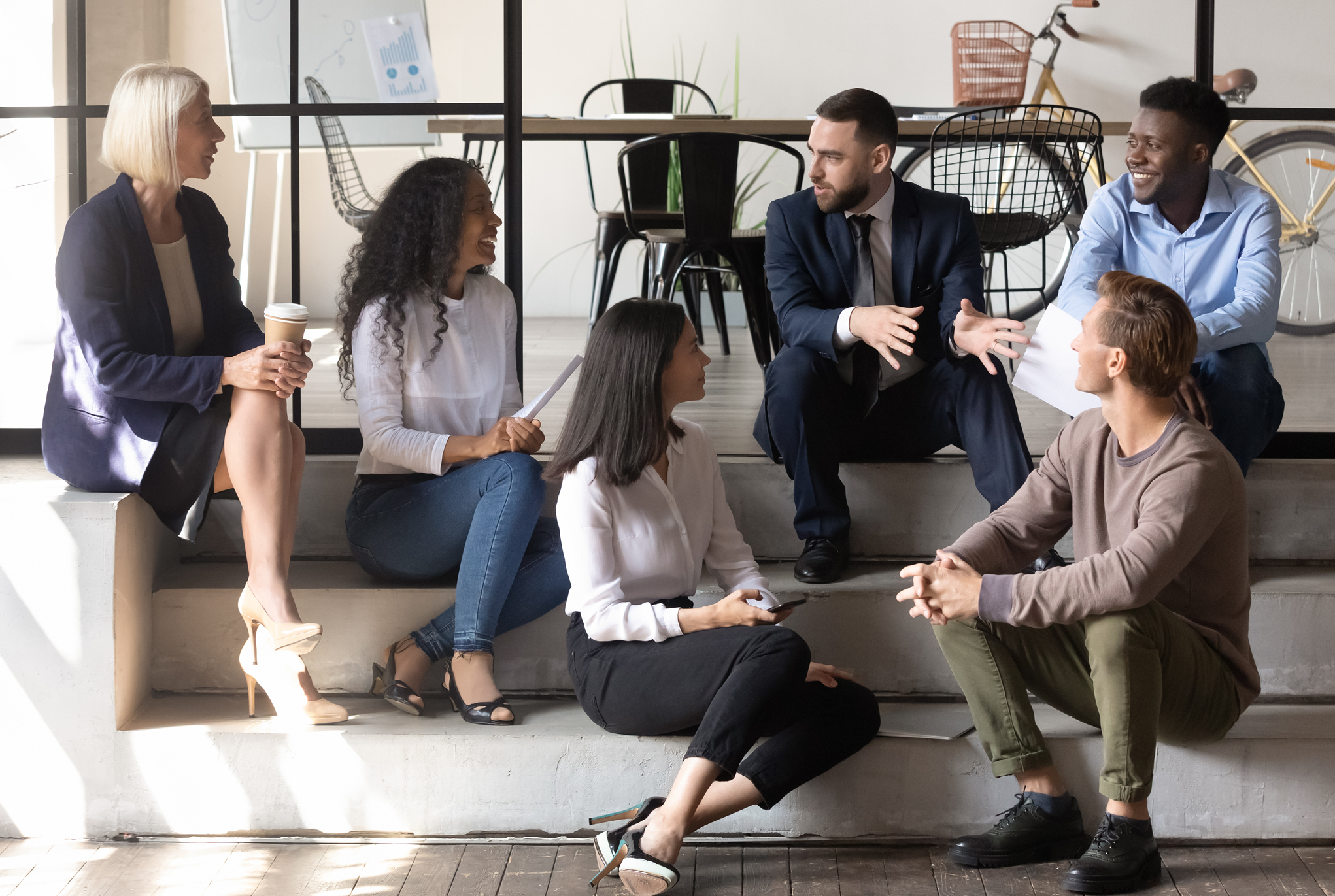 A group of employees sitting on steps talking to each other. 
