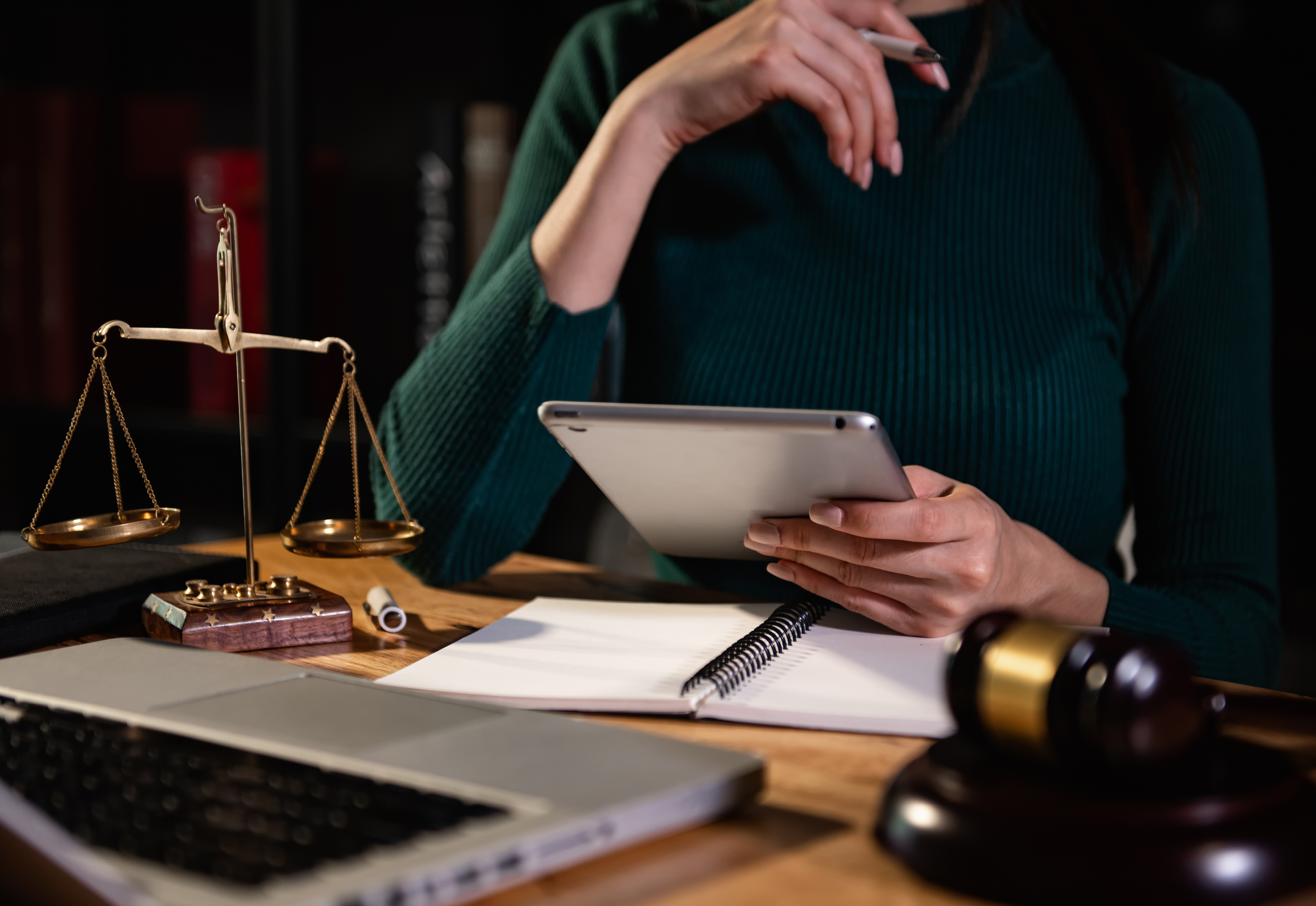 A person sitting at a desk with a tablet, notebook, laptop, and a scale of justice