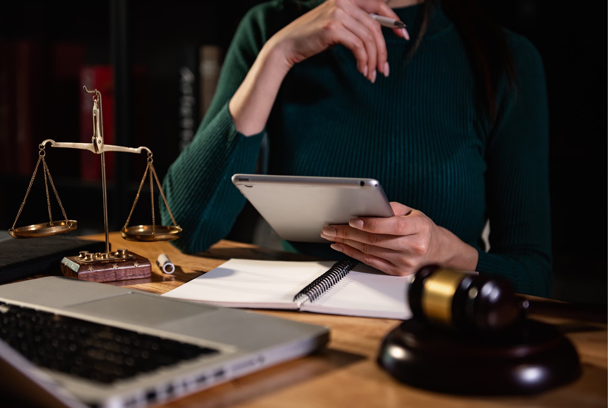 A person sitting at a desk with a tablet, notebook, laptop, and a scale of justice