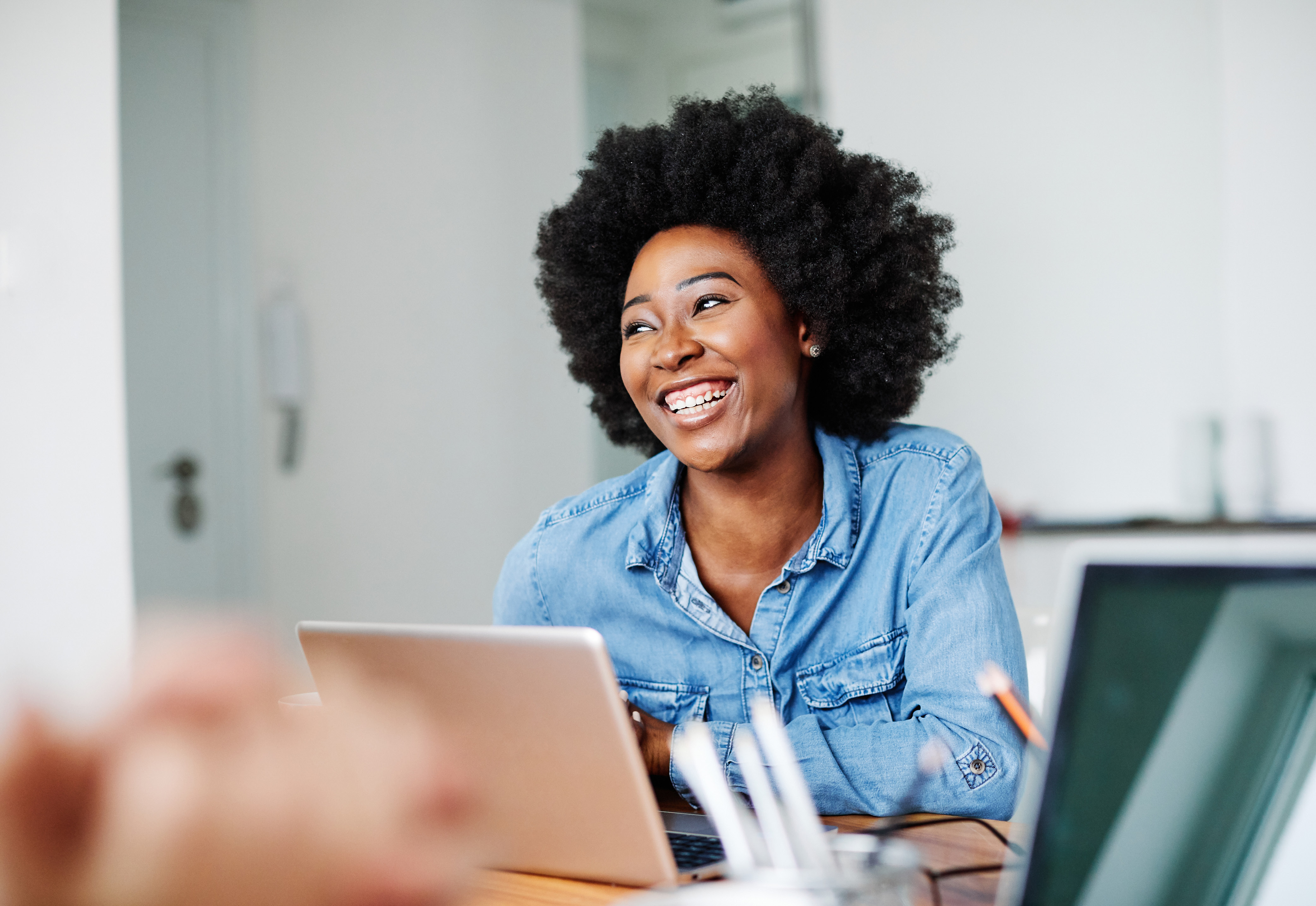 A woman in a denim shirt sitting at a desk with a laptop