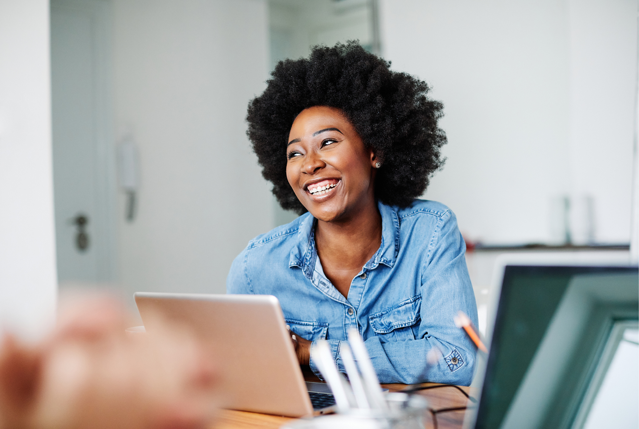 A woman in a denim shirt sitting at a desk with a laptop