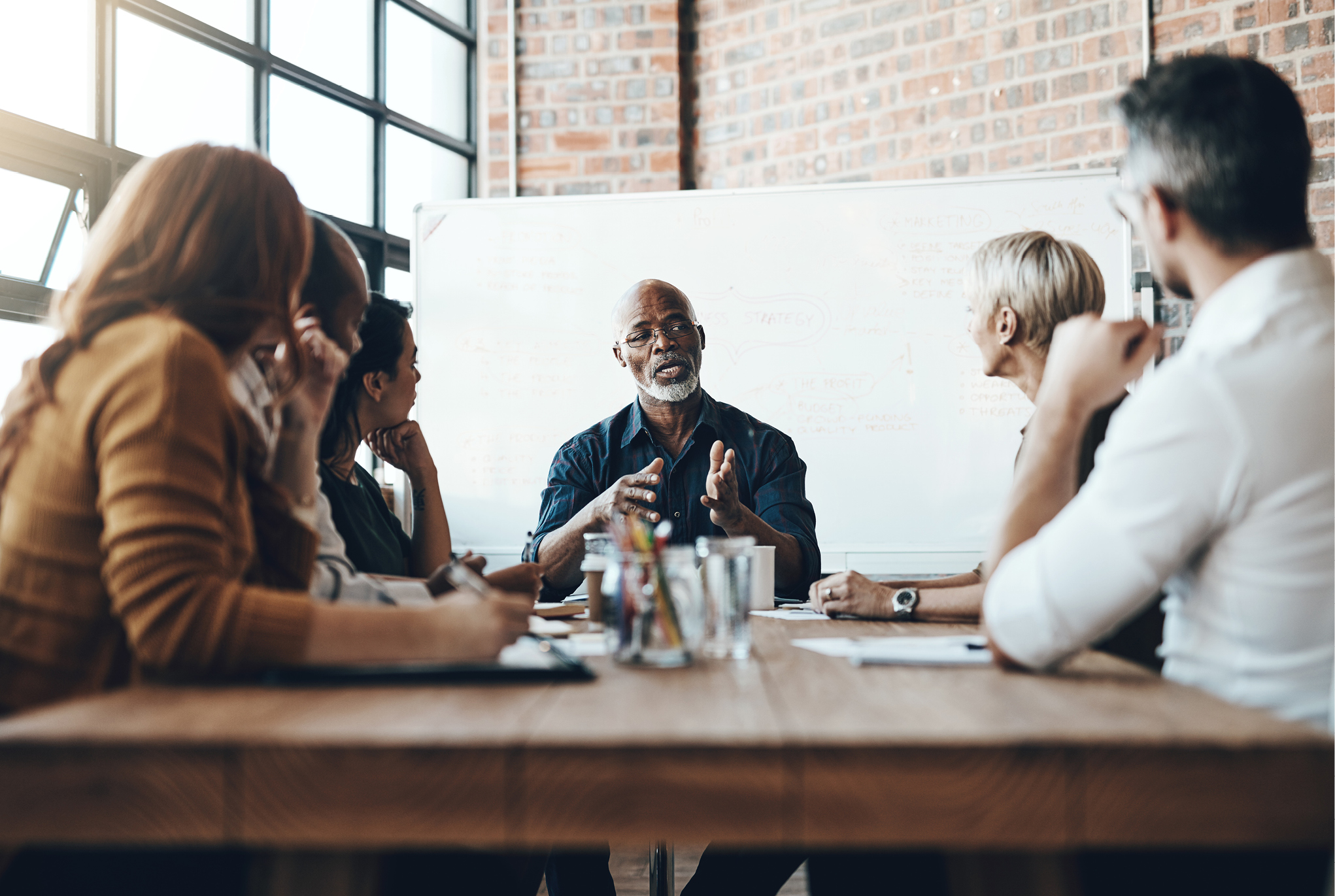 A group of people sitting around a table with a whiteboard in the background