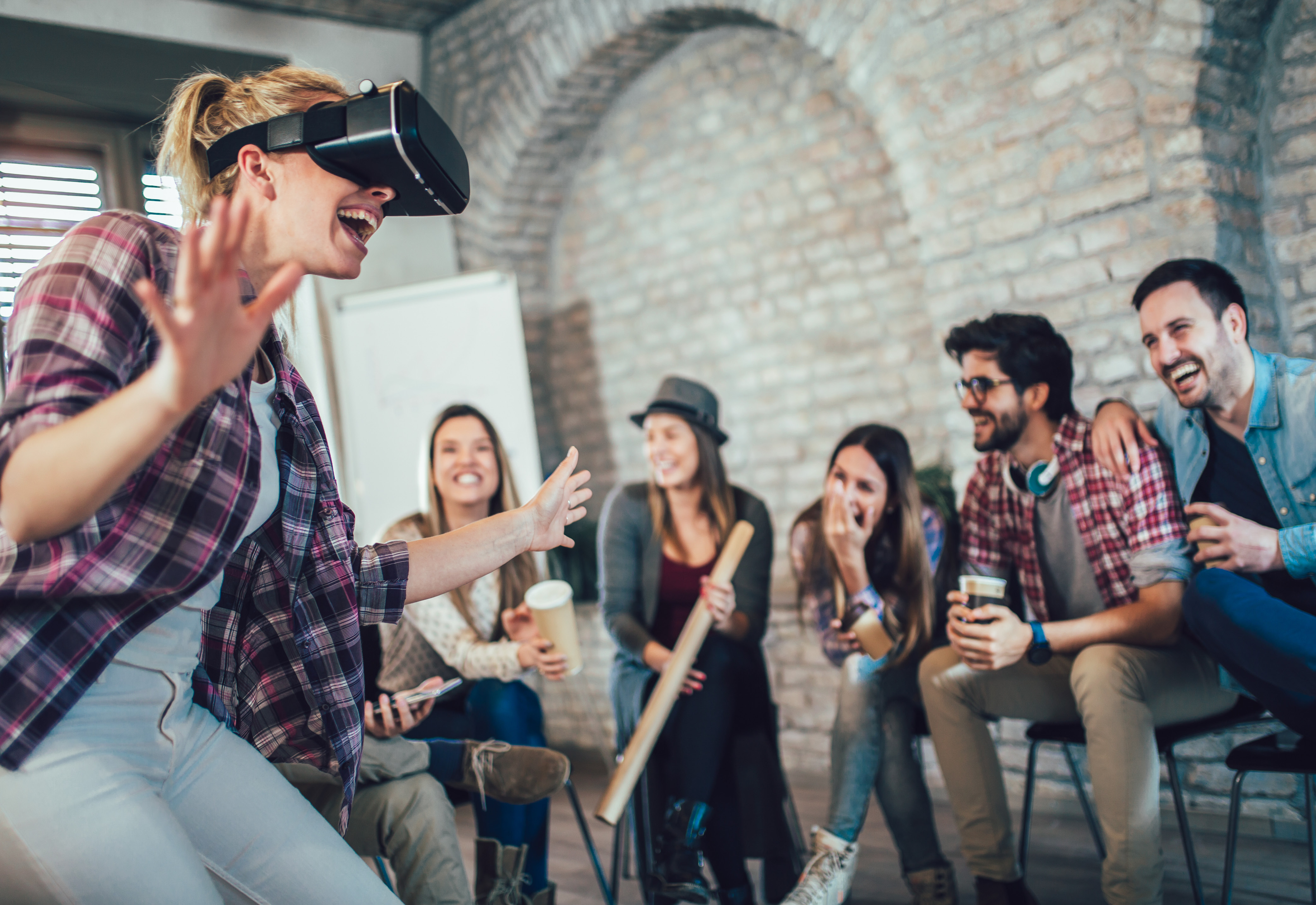 A group of people sitting while one person uses a virtual reality headset