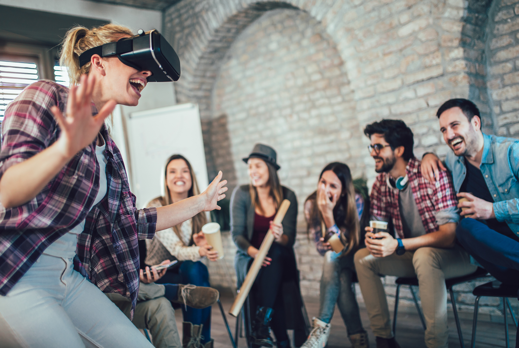 A group of people sitting while one person uses a virtual reality headset