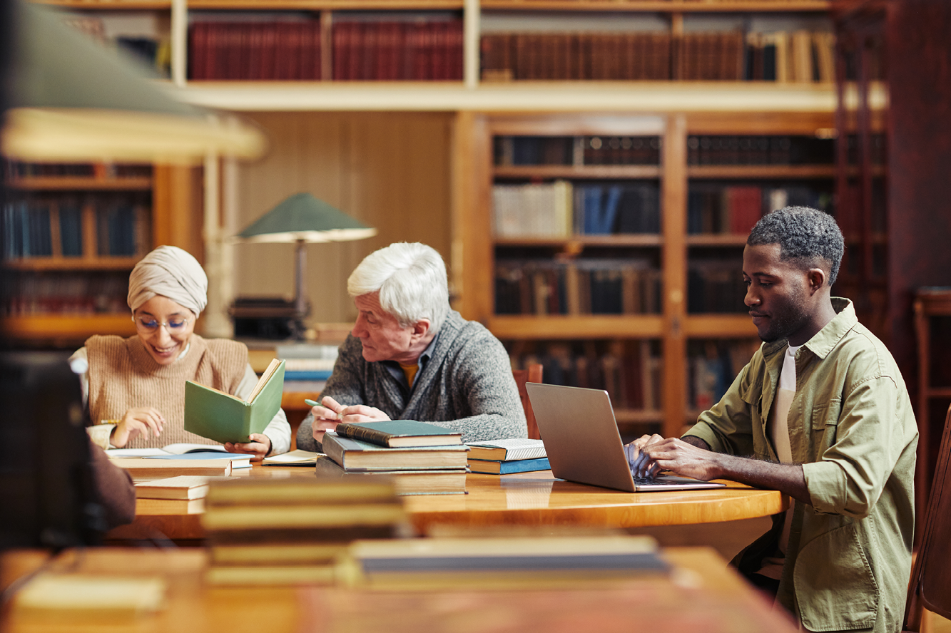 A group of three people sitting at a table with books and a laptop