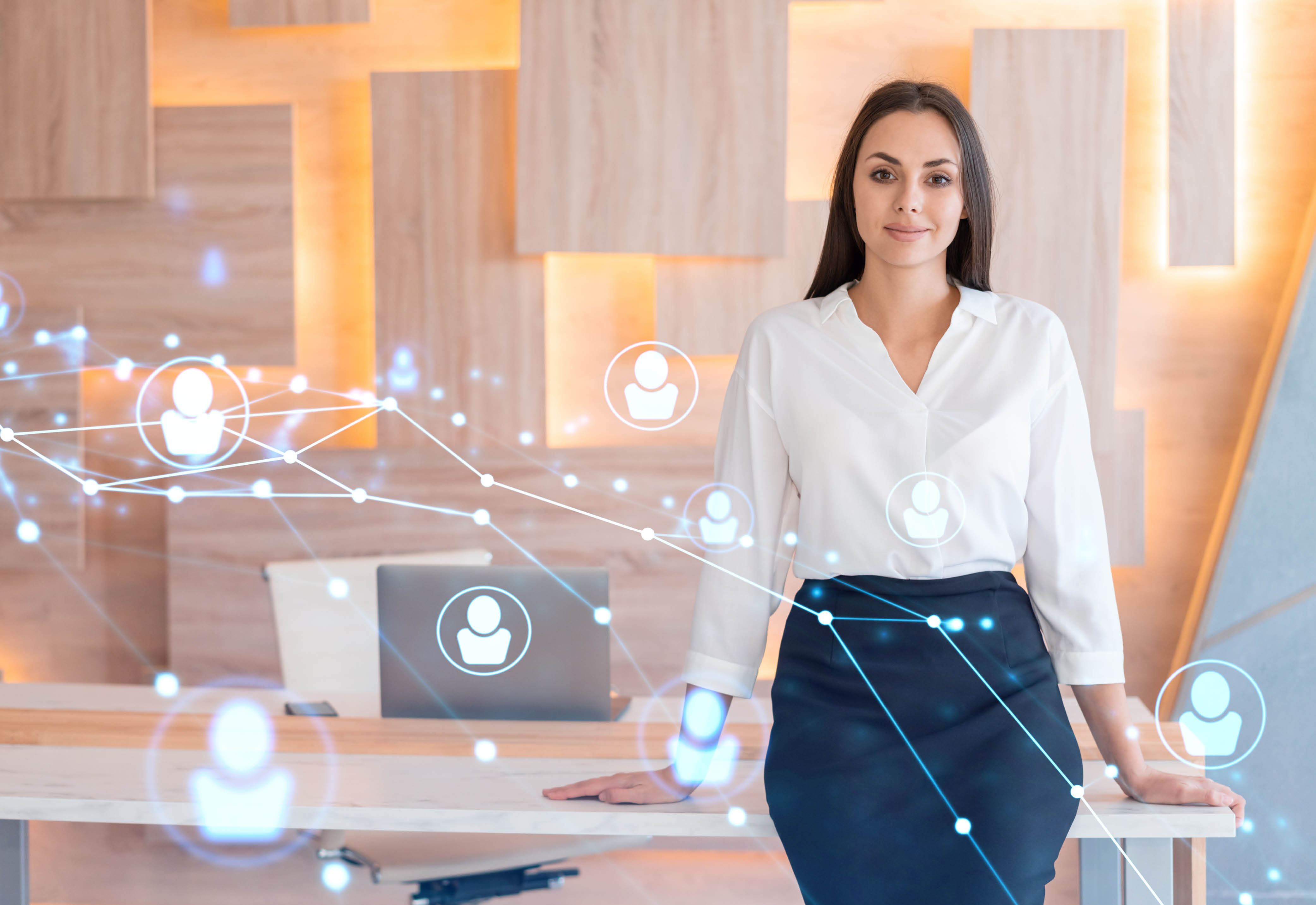 A woman in business attire standing in front of a desk with graphics of people icons over the photo.