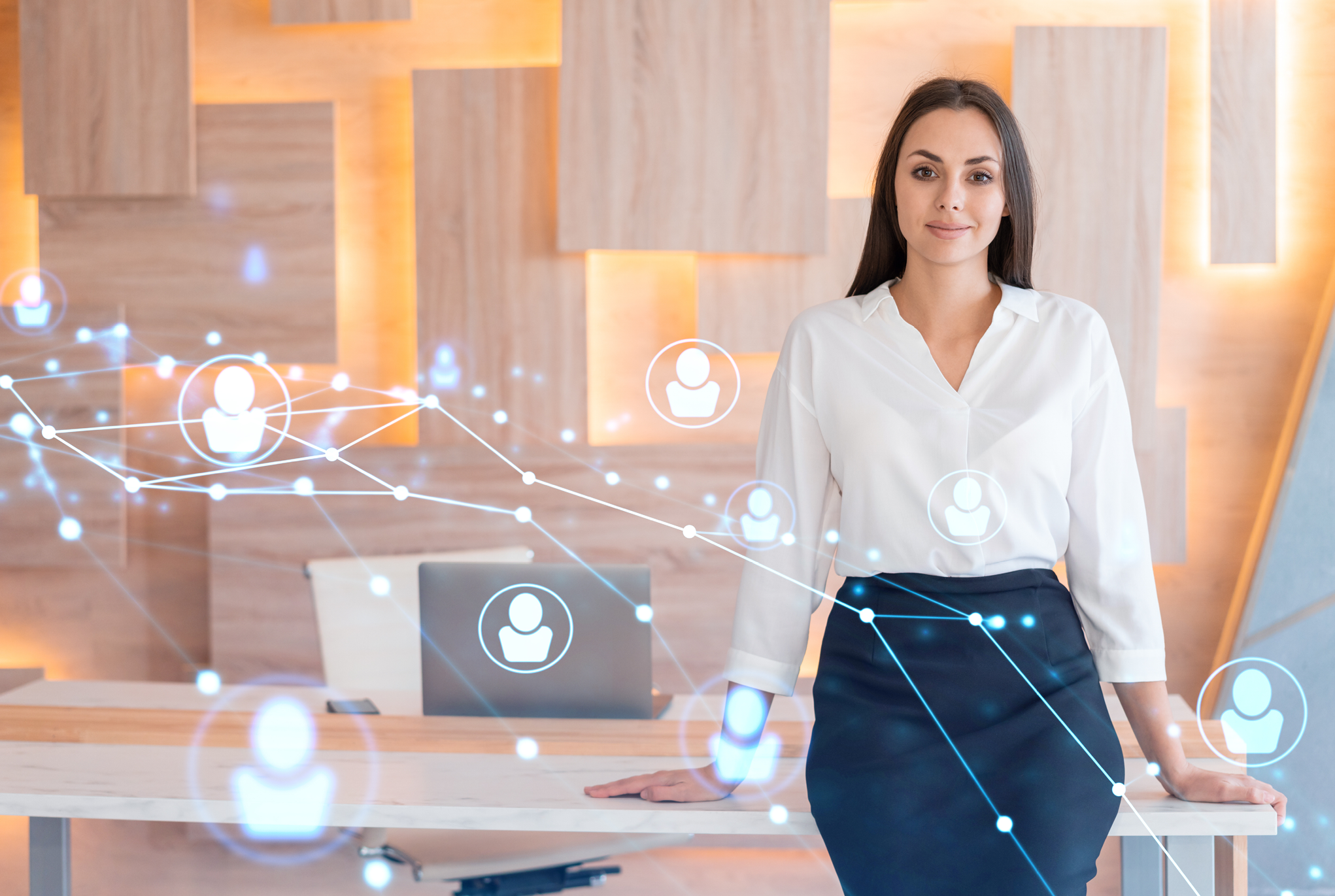 A woman in business attire standing in front of a desk with graphics of people icons over the photo. 