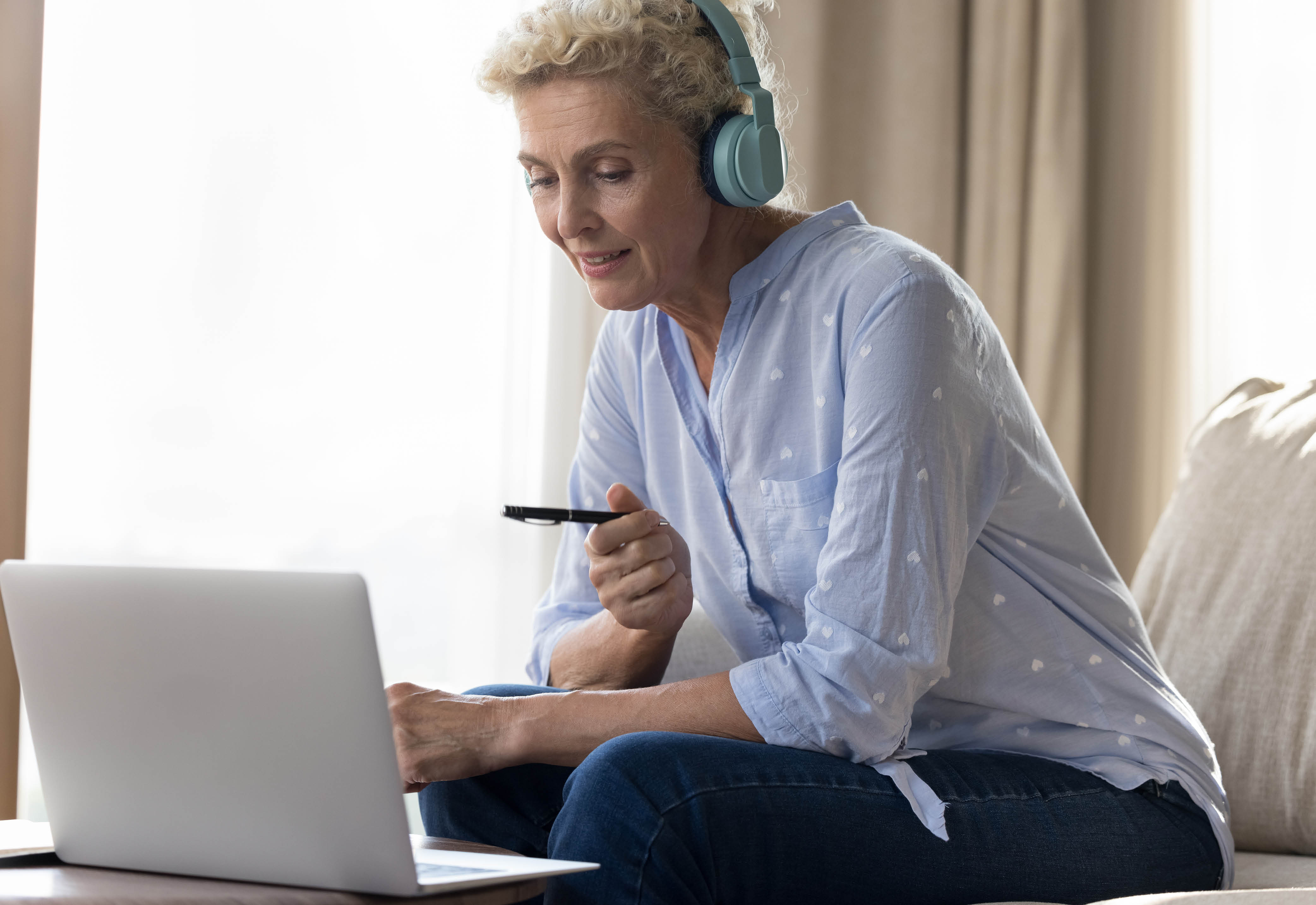 Woman sitting on a couch wearing headphones while using her laptop