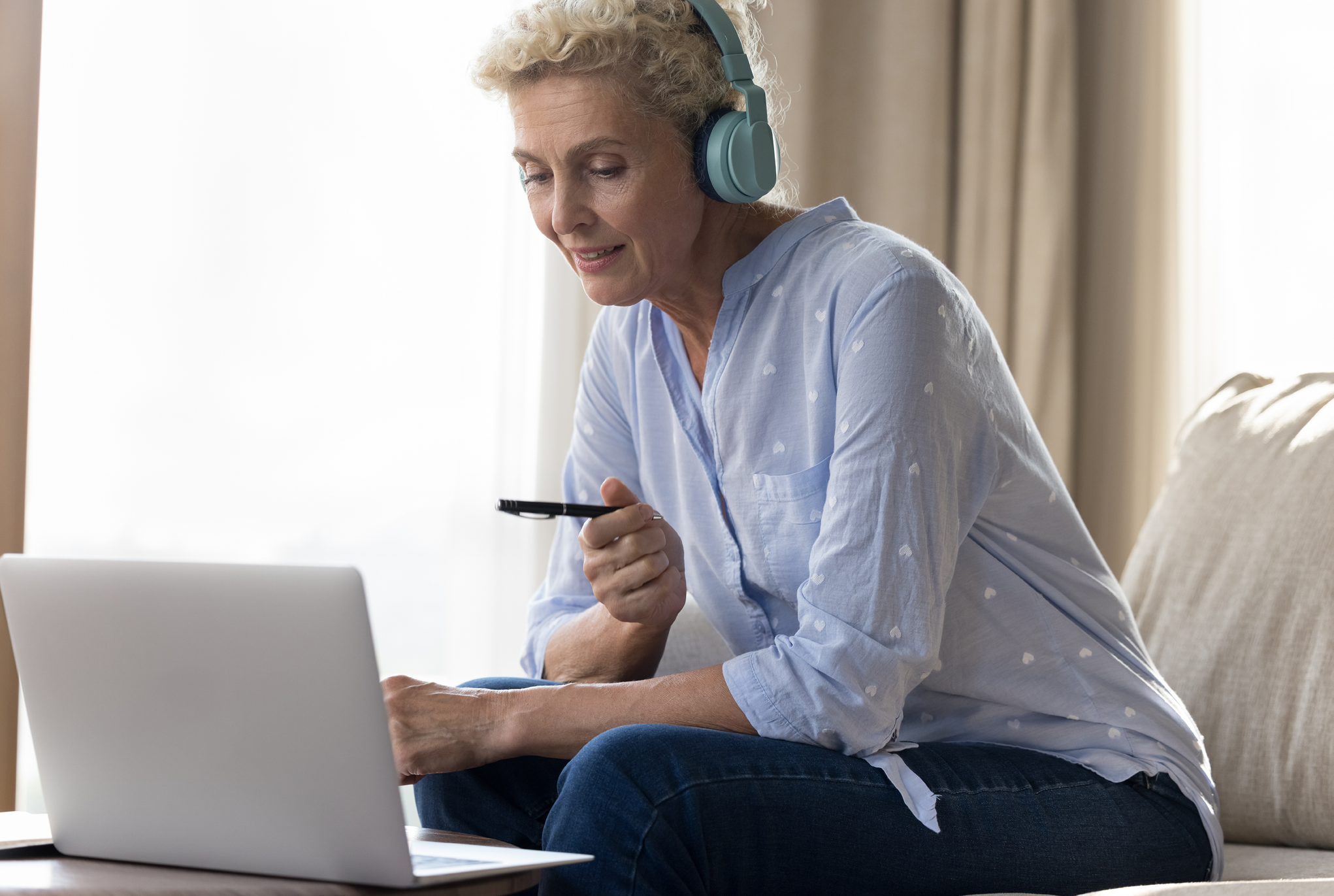 Woman sitting on a couch wearing headphones while using her laptop