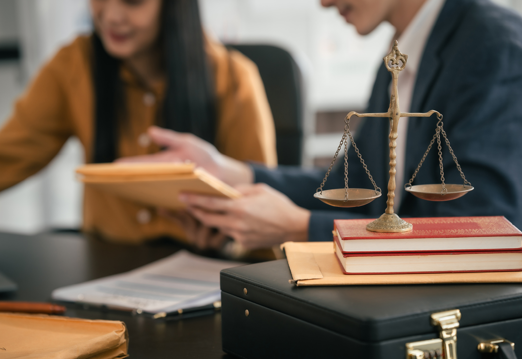 Two people sitting at a desk with a stack of books and the scales of justice