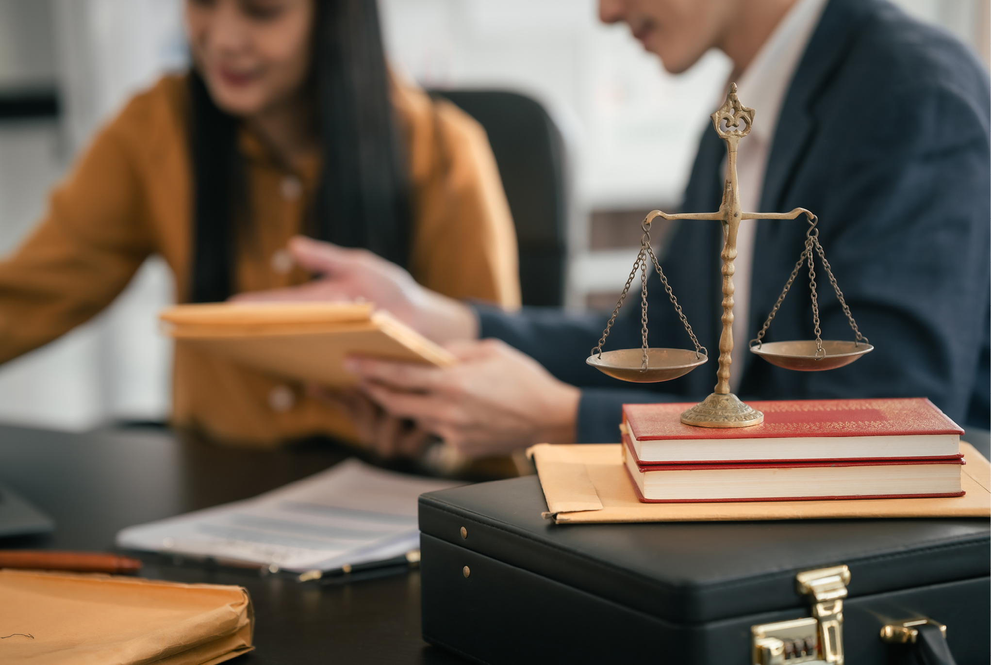 Two people sitting at a desk with a stack of books and the scales of justice