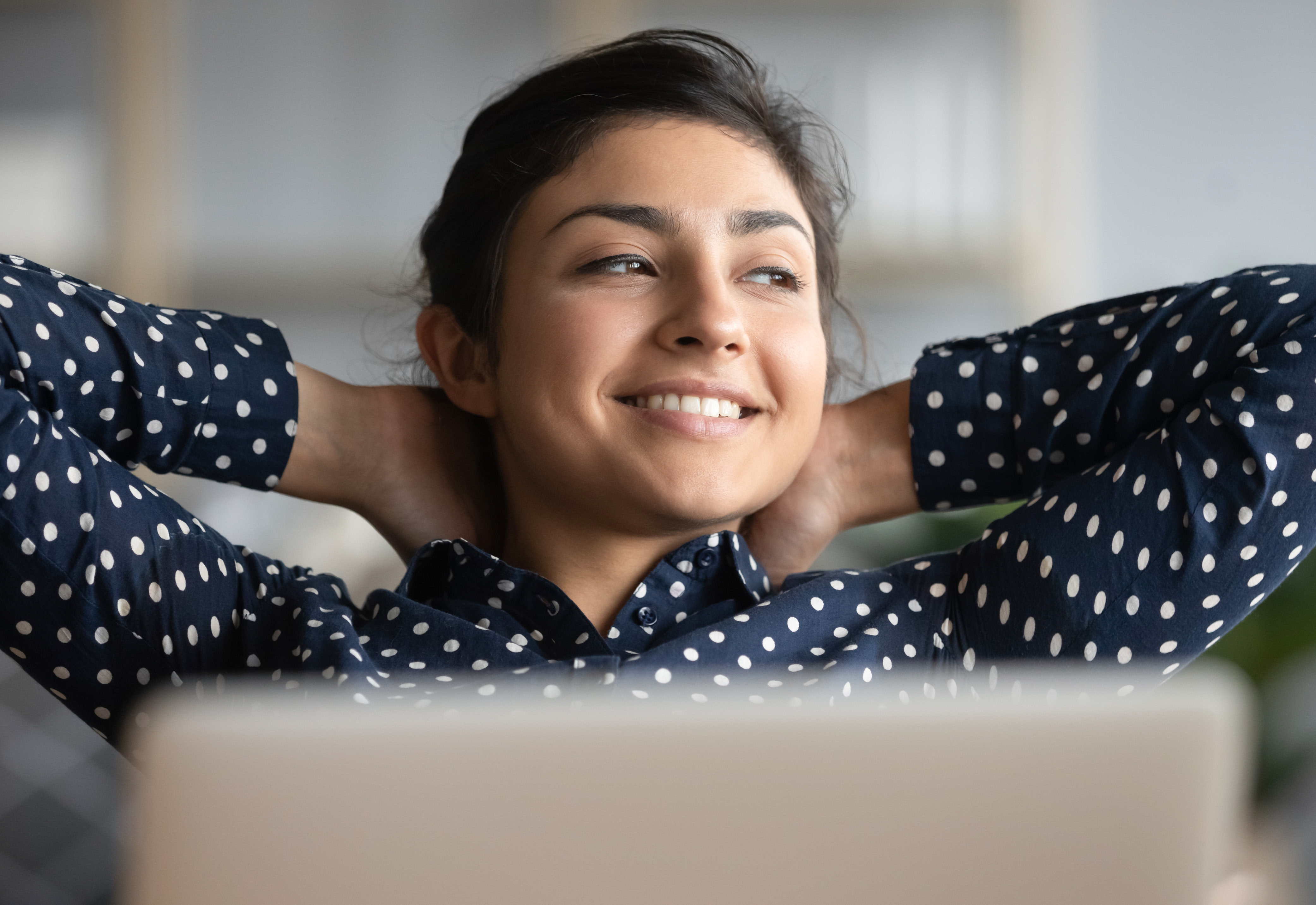 A woman in a polka dot blouse relaxing with her hands behind her head