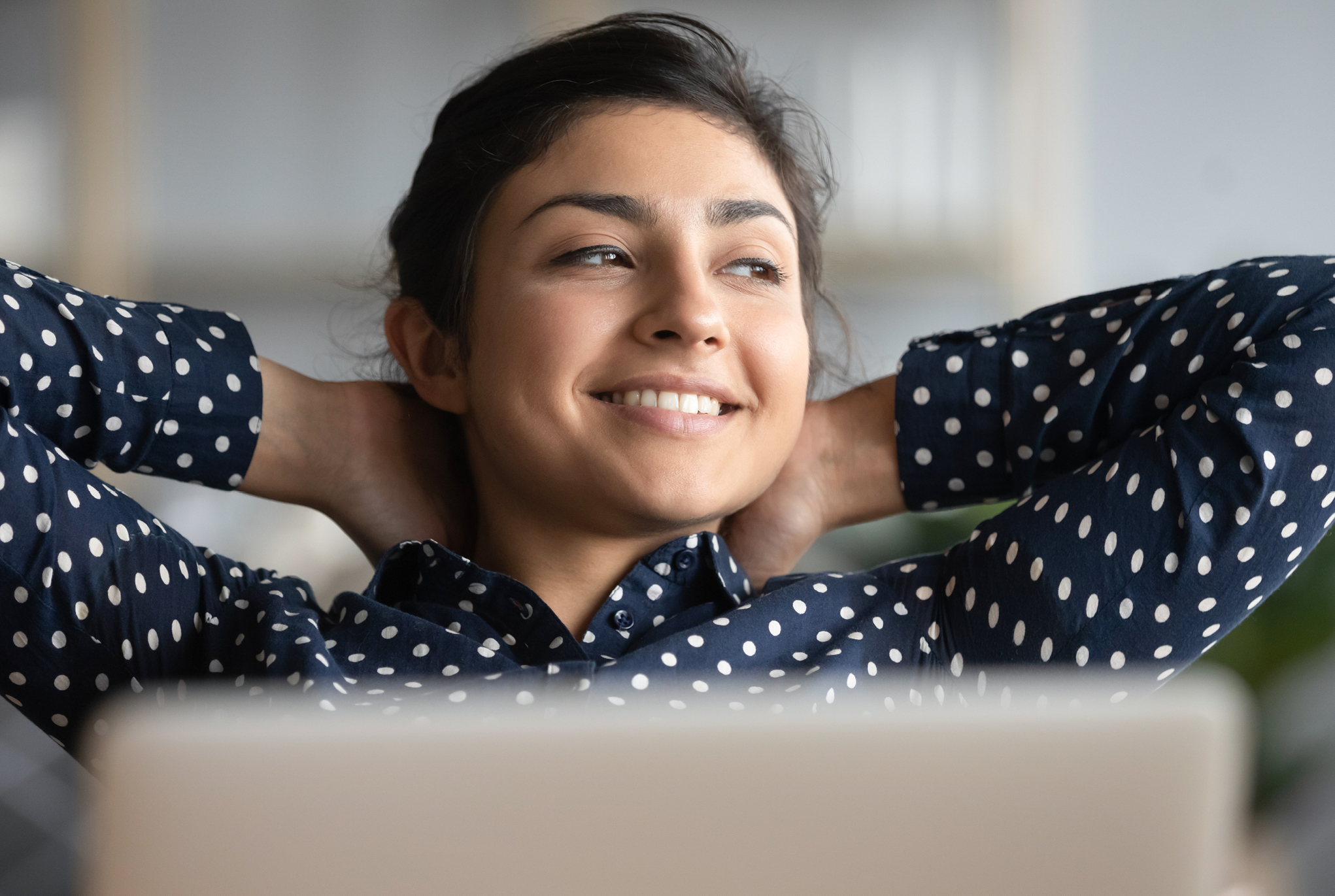 A woman in a polka dot blouse relaxing with her hands behind her head