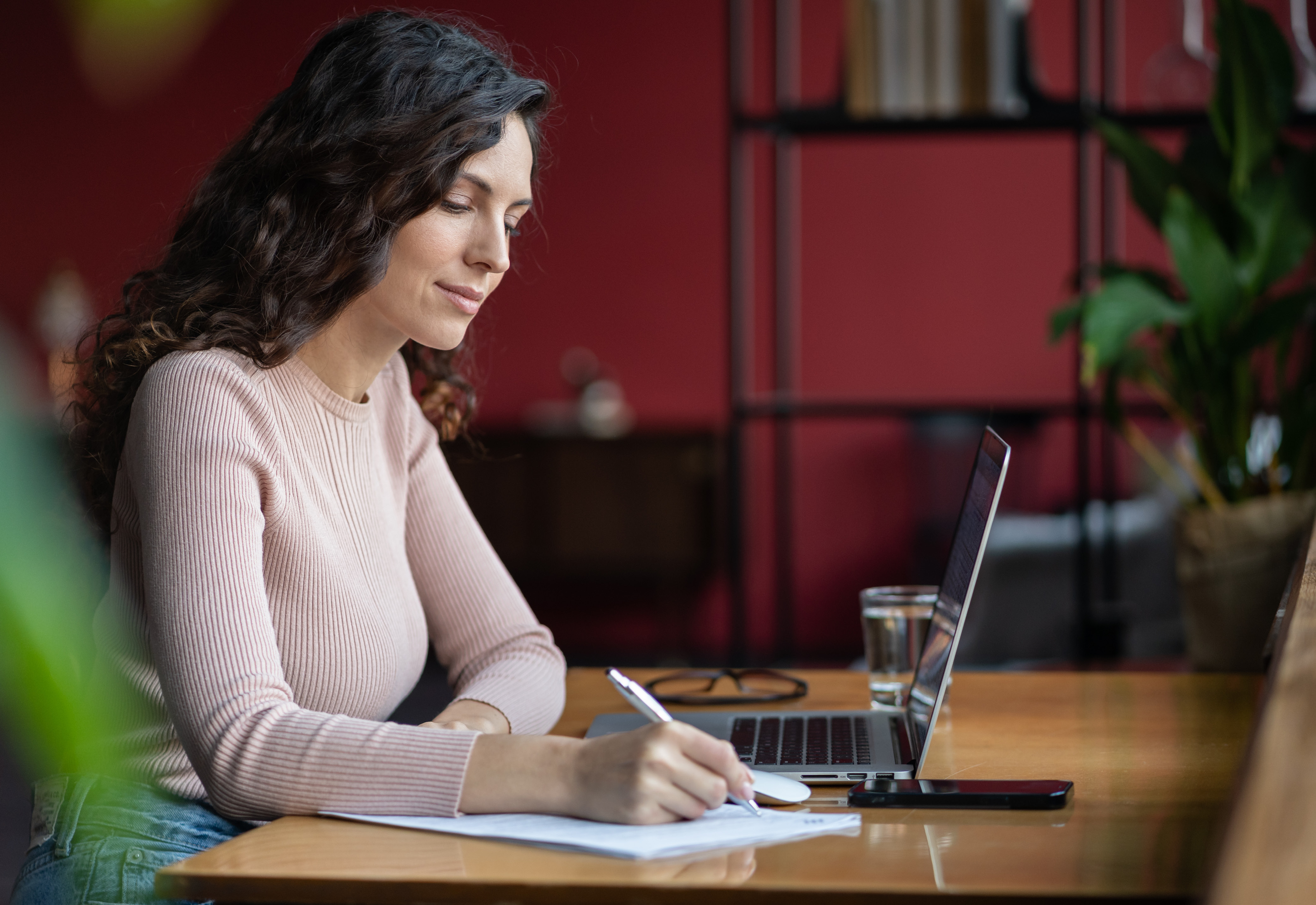 A woman sitting in front of her laptop at a desk taking notes