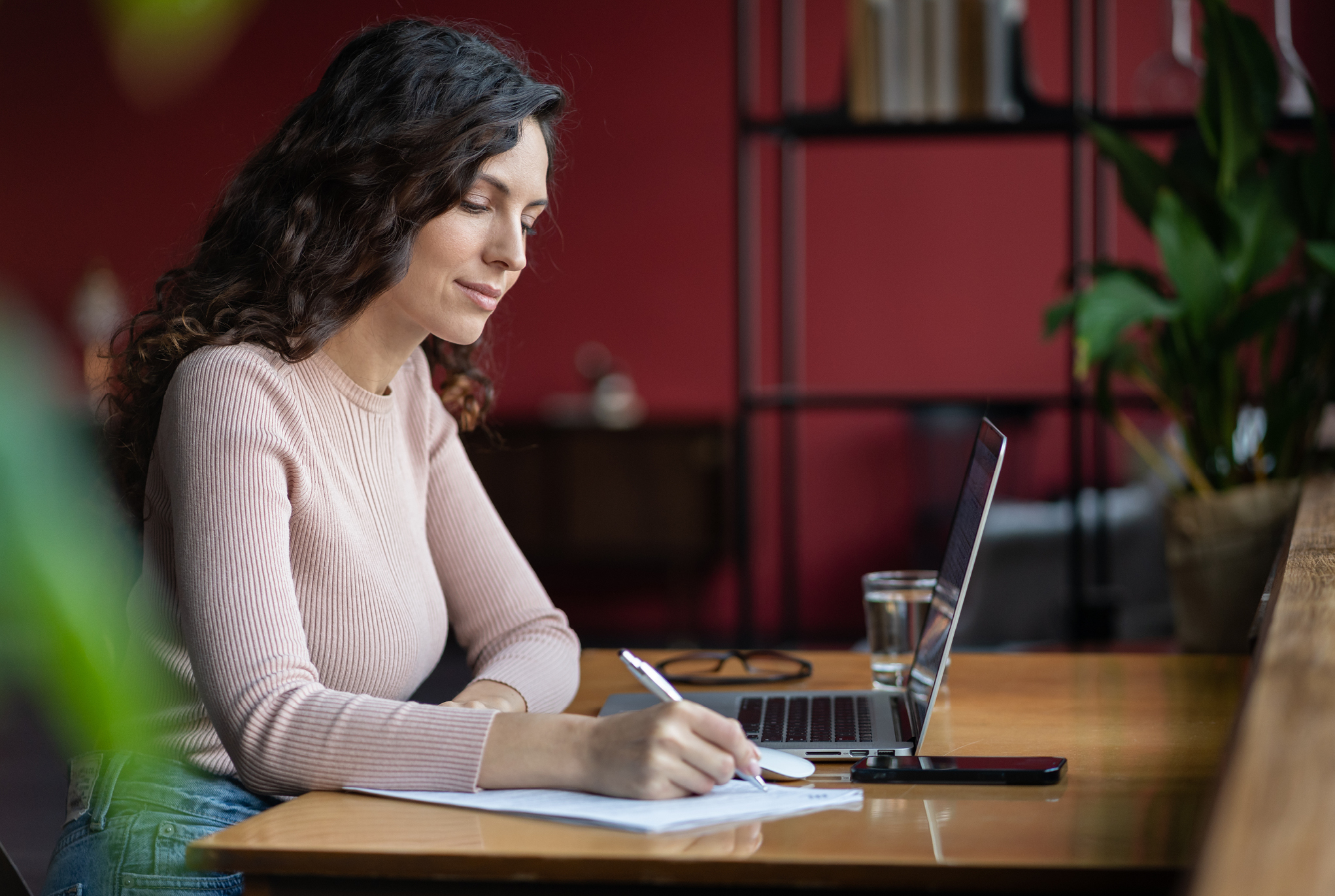 A woman sitting in front of her laptop at a desk taking notes