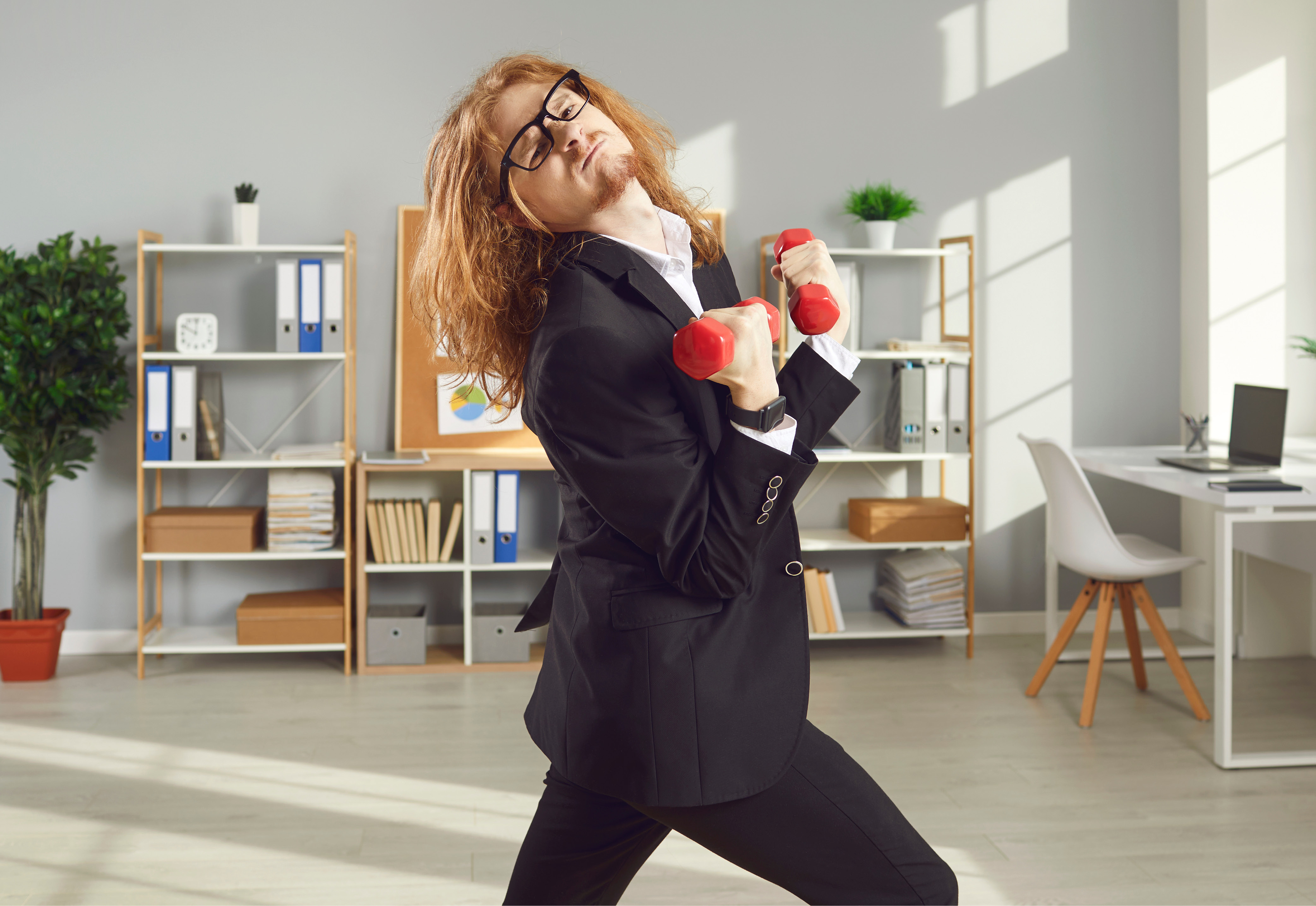 An employee wearing a business suit and glasses lifting weights