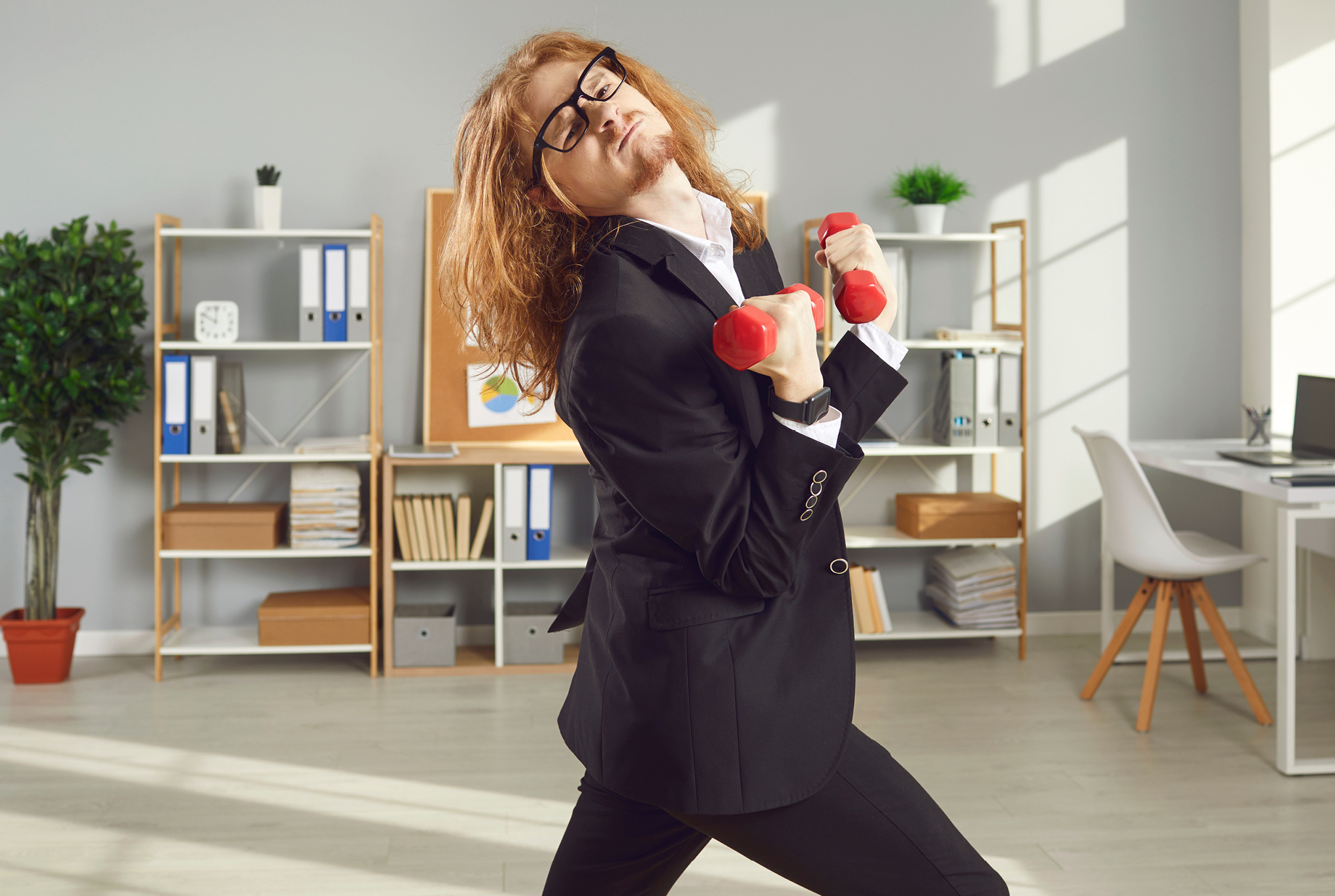 An employee wearing a business suit and glasses lifting weights
