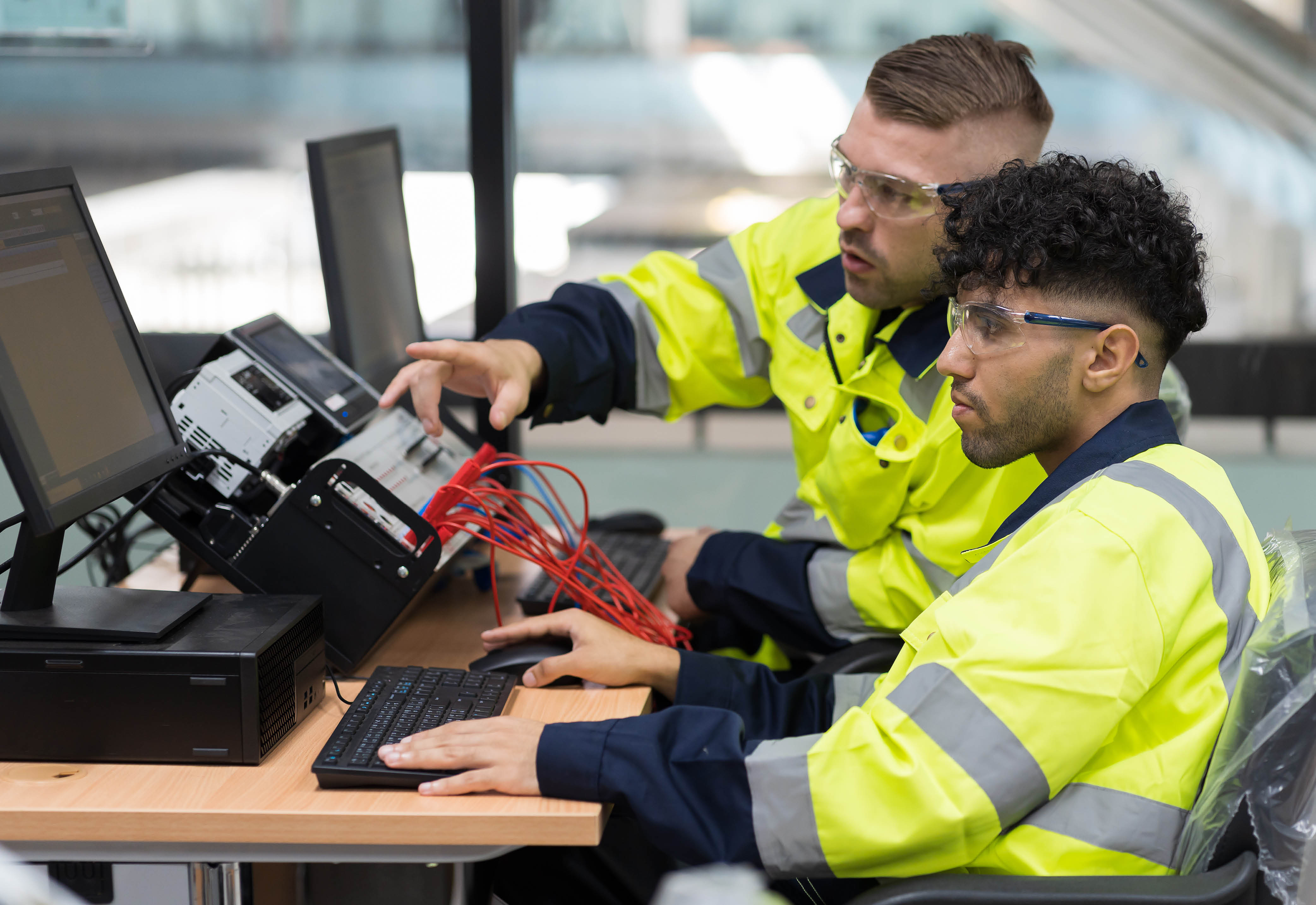 Two men wearing protective glasses and yellow jackets working with equipment