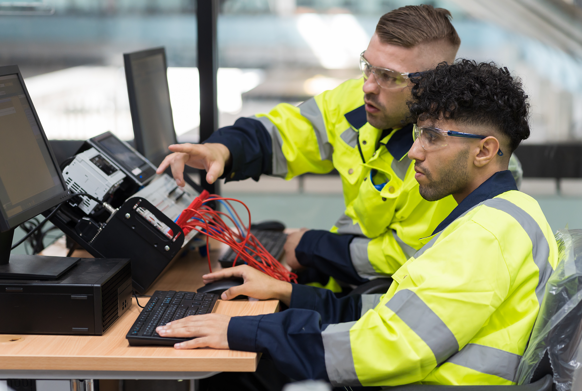 Two men wearing protective glasses and yellow jackets working with equipment