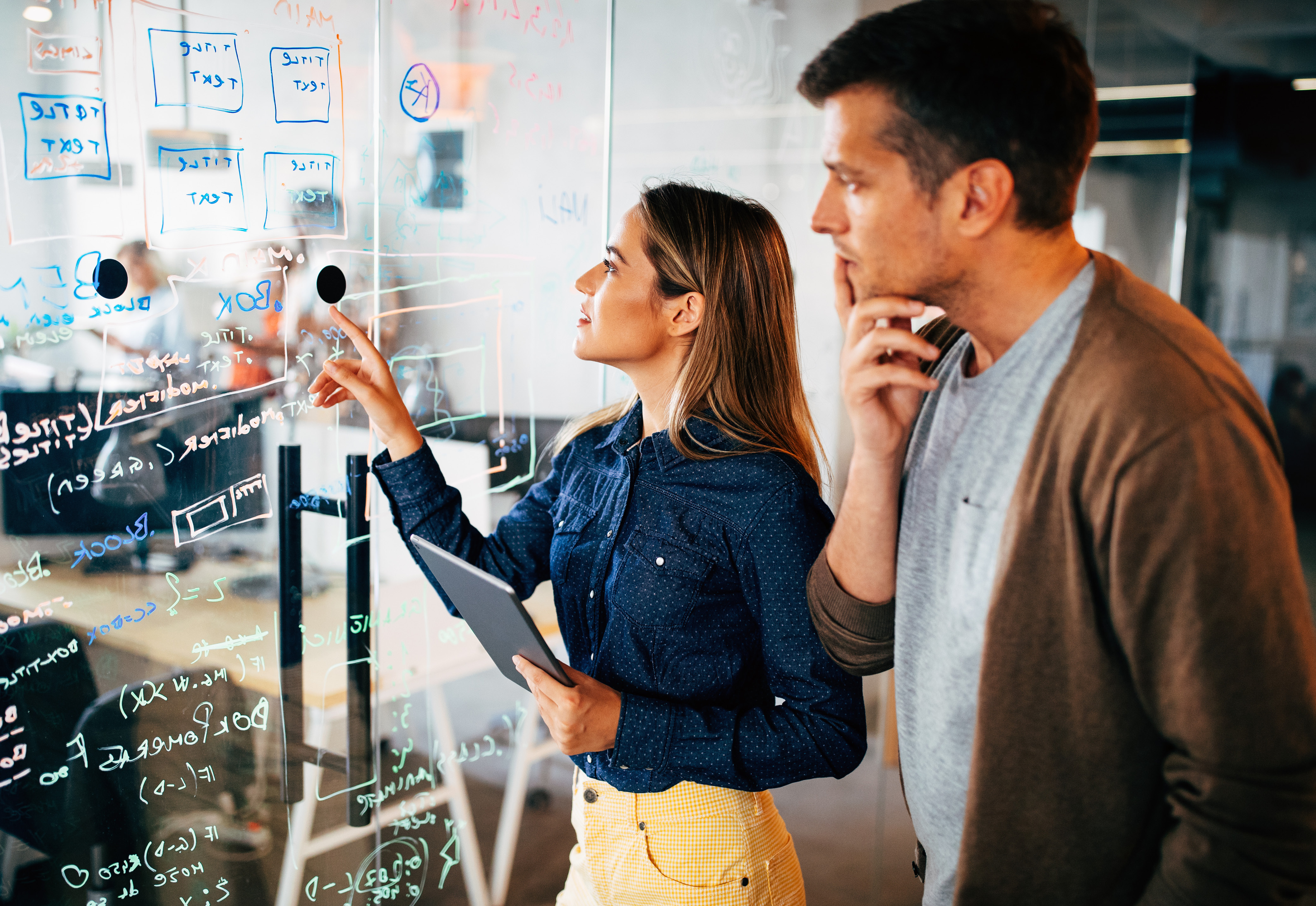 Two people looking at notes on a board in an office