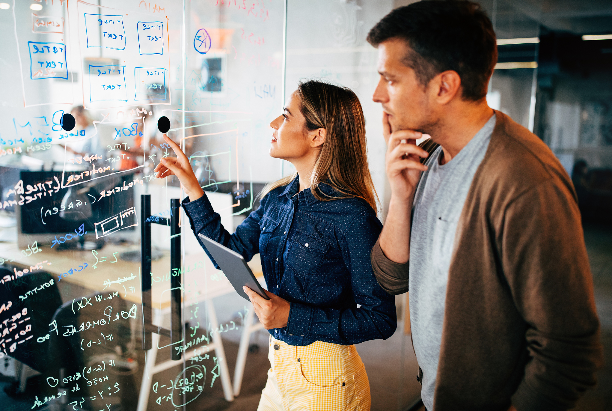 Two people looking at notes on a board in an office