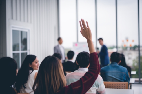 A woman raising her hand to ask a question during a presentation