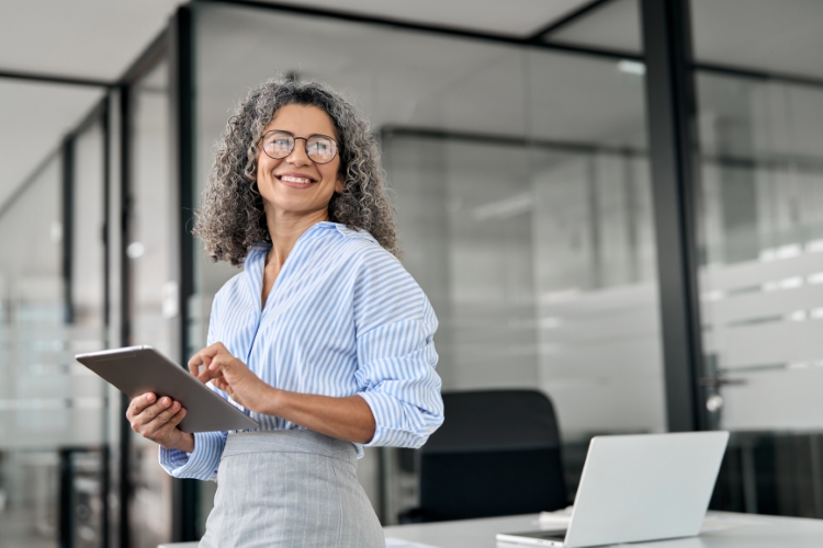A gray and black curly haired professional woman at a desk with a tablet