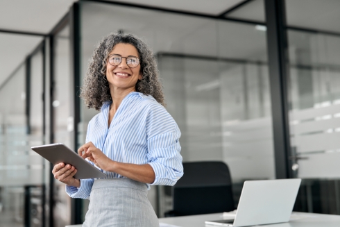 A gray and black curly haired professional woman at a desk with a tablet