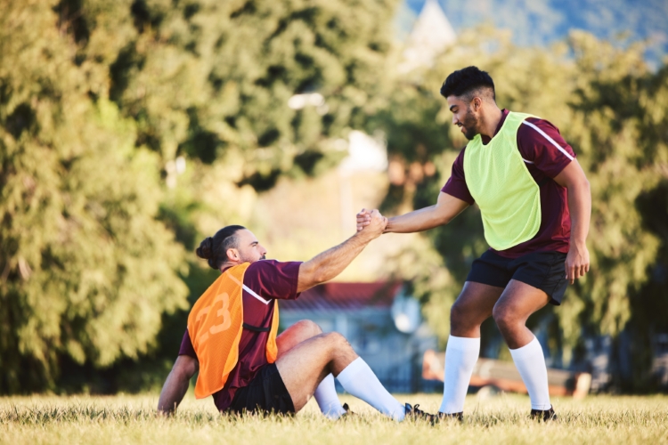 A soccer player helping his teammate up