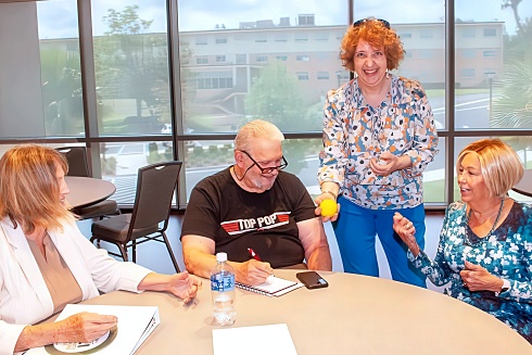 A group of happy older adults sit around a round table discussing something